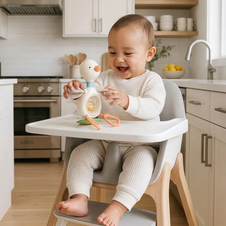 Happy baby in high chair playing with Itzy Ritzy Twist and Bop Goose toy in modern kitchen