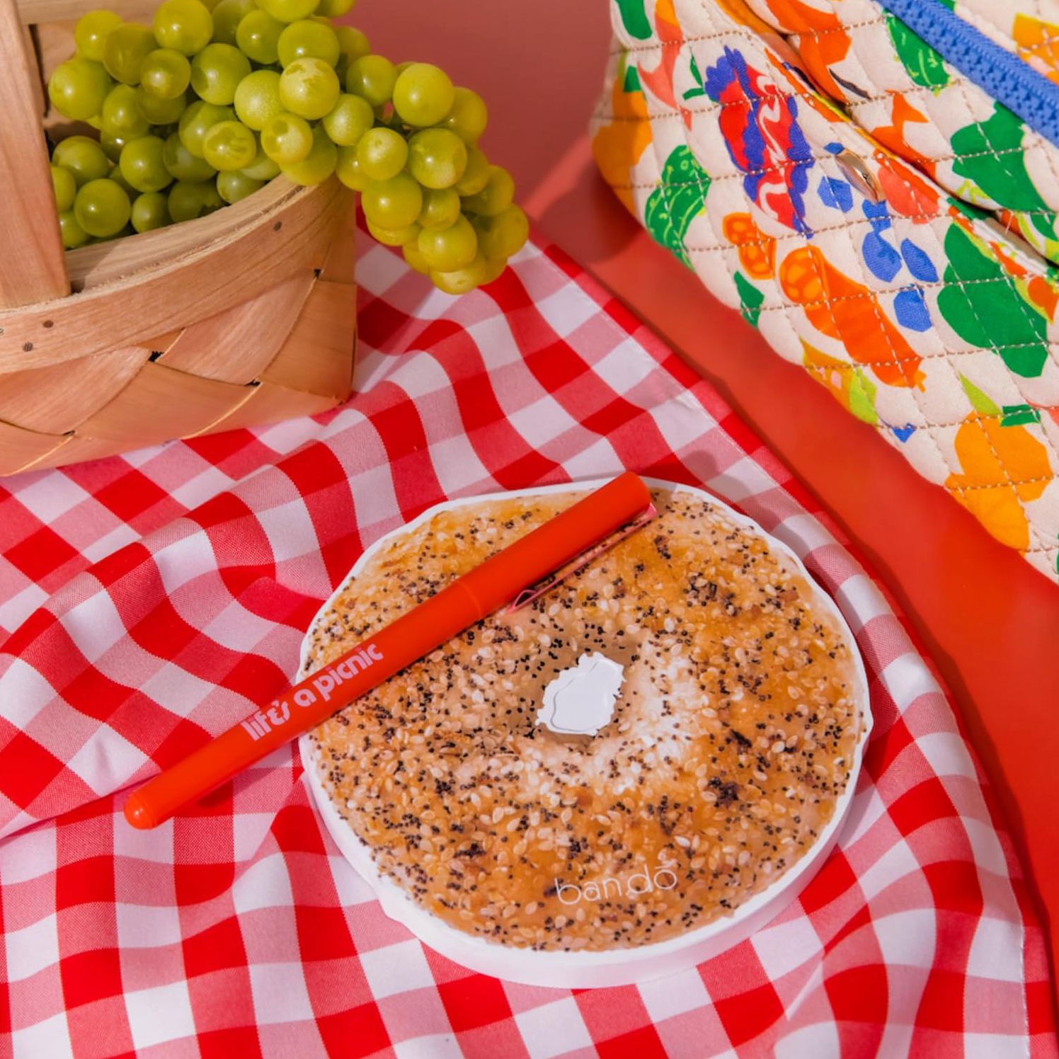 Ban.do bagel-shaped notepad on red gingham picnic blanket with grapes and colorful bag