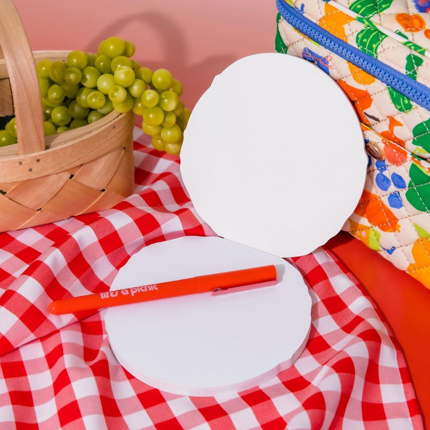 White bagel-shaped notepad with orange pen on red gingham picnic cloth with basket