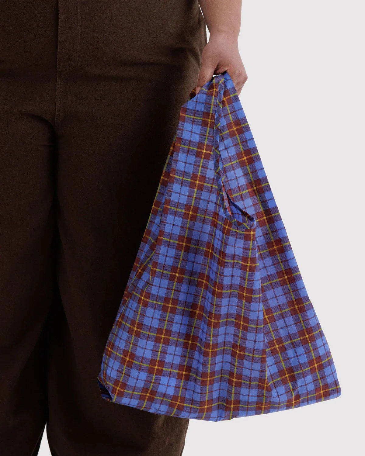 Hand holding a blue tartan plaid reusable Baggu tote bag against neutral background