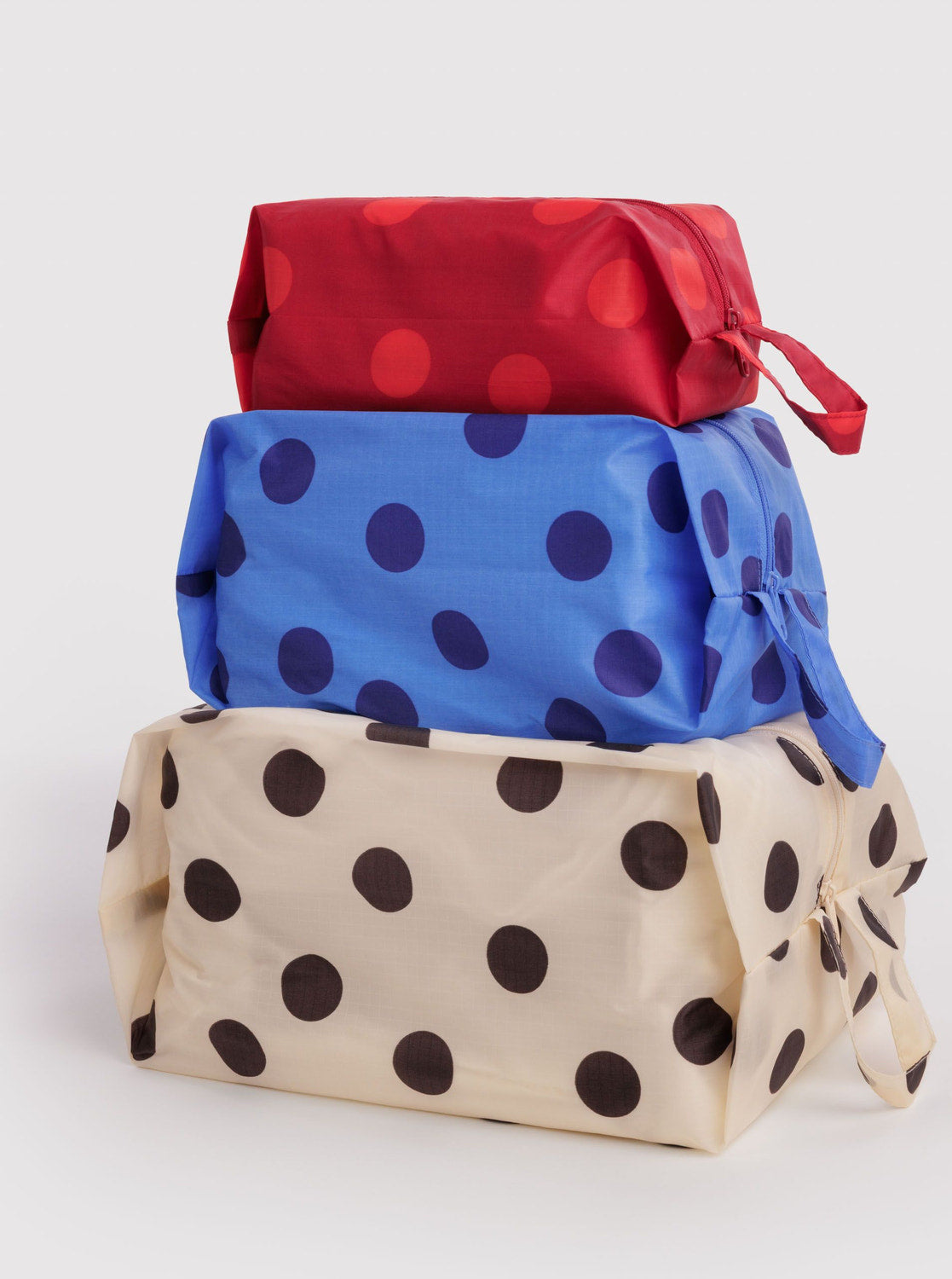 Three polka dot zip pouches stacked in red, blue, and cream with zipper closures
