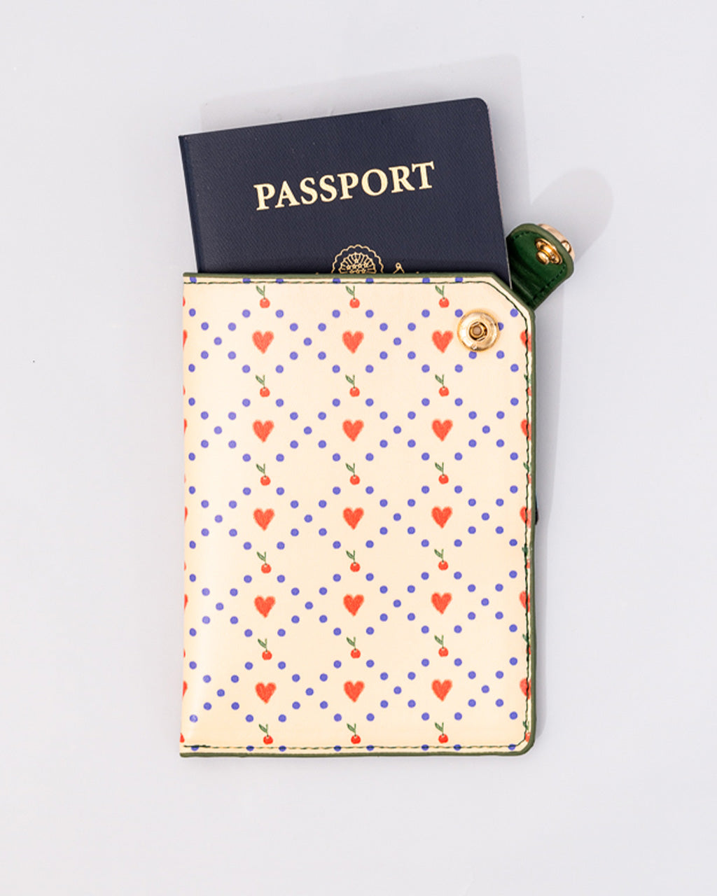 Cream passport holder with red hearts, cherries, and blue polka dots pattern, holding a navy passport