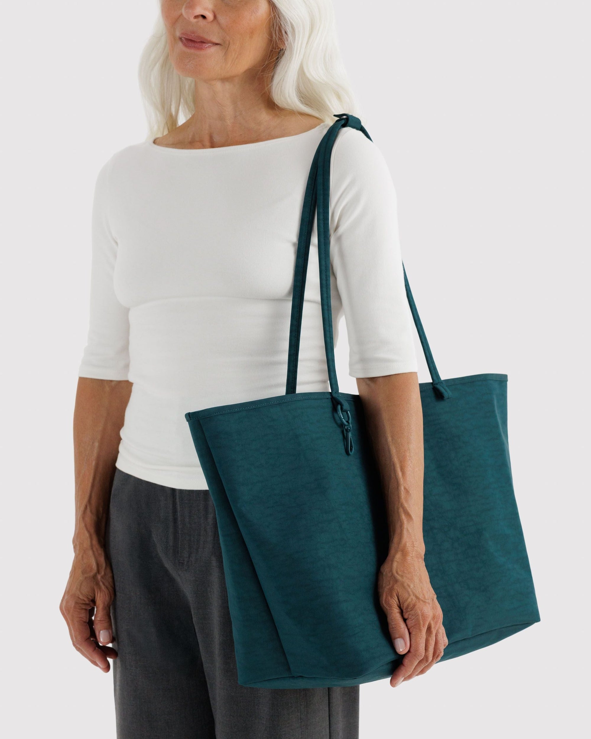 Older woman with white hair carrying a large deep teal nylon tote bag on her shoulder