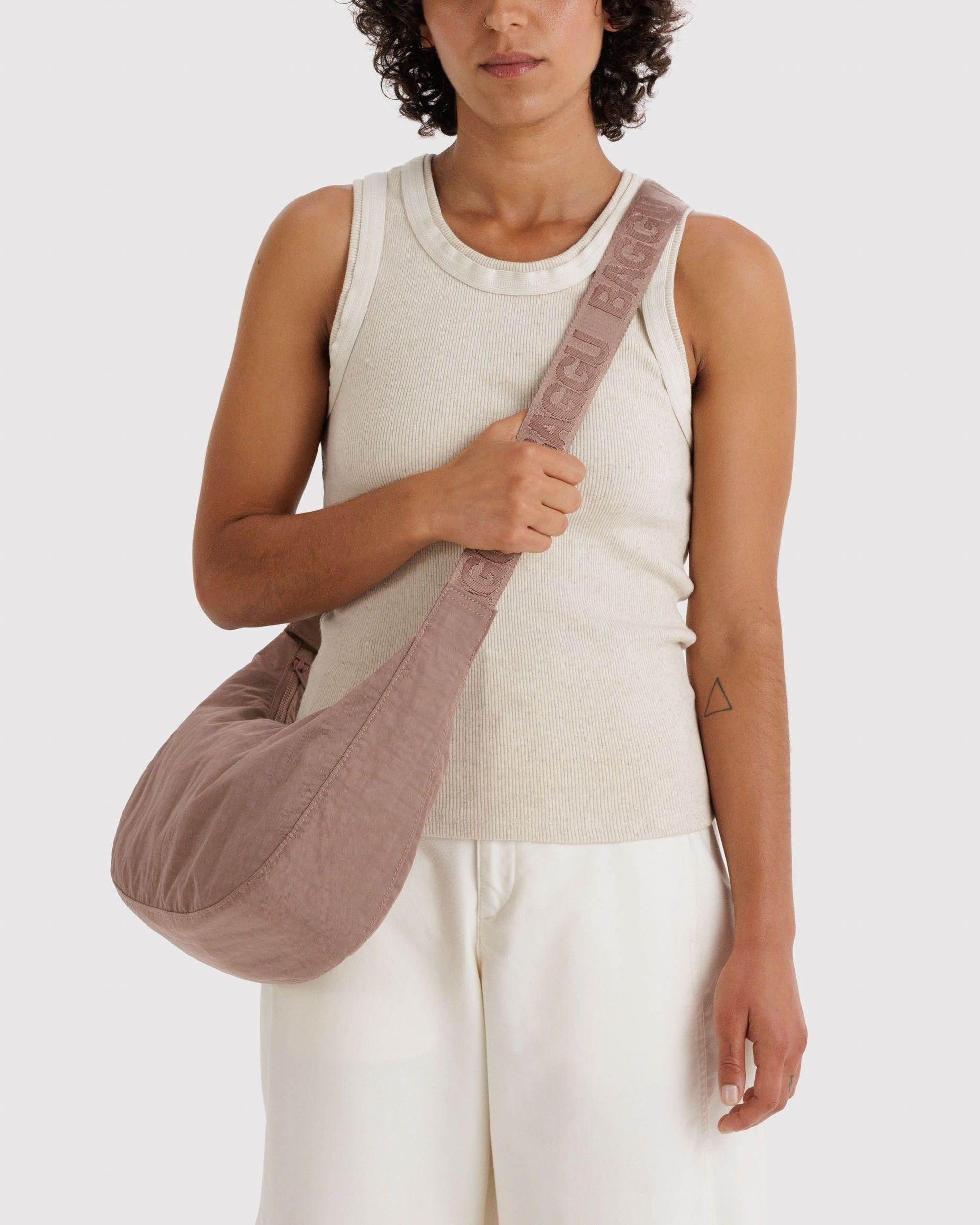 Model wearing cream tank top carrying Baggu Medium Nylon Crescent Bag in Toasted Almond crossbody