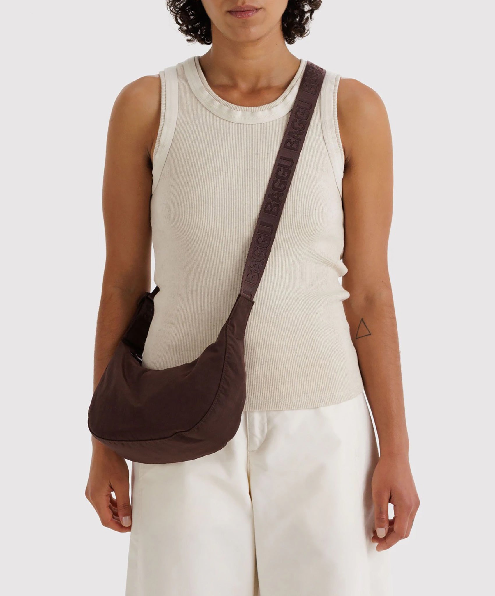 Model wearing Baggu Small Nylon Crescent Bag in dark brown as crossbody over cream ribbed tank top