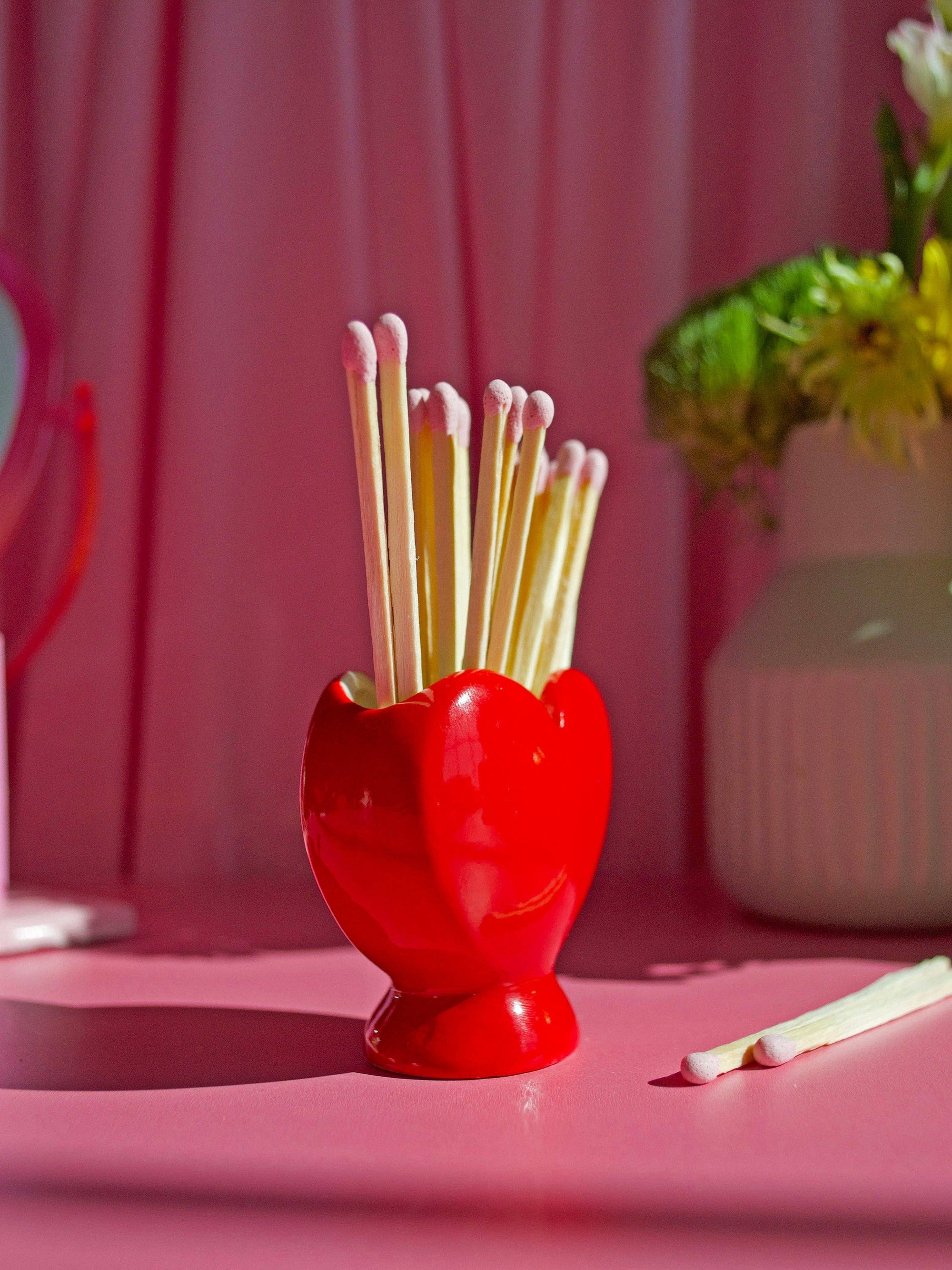Red heart-shaped match striker holder with wooden matches on pink surface