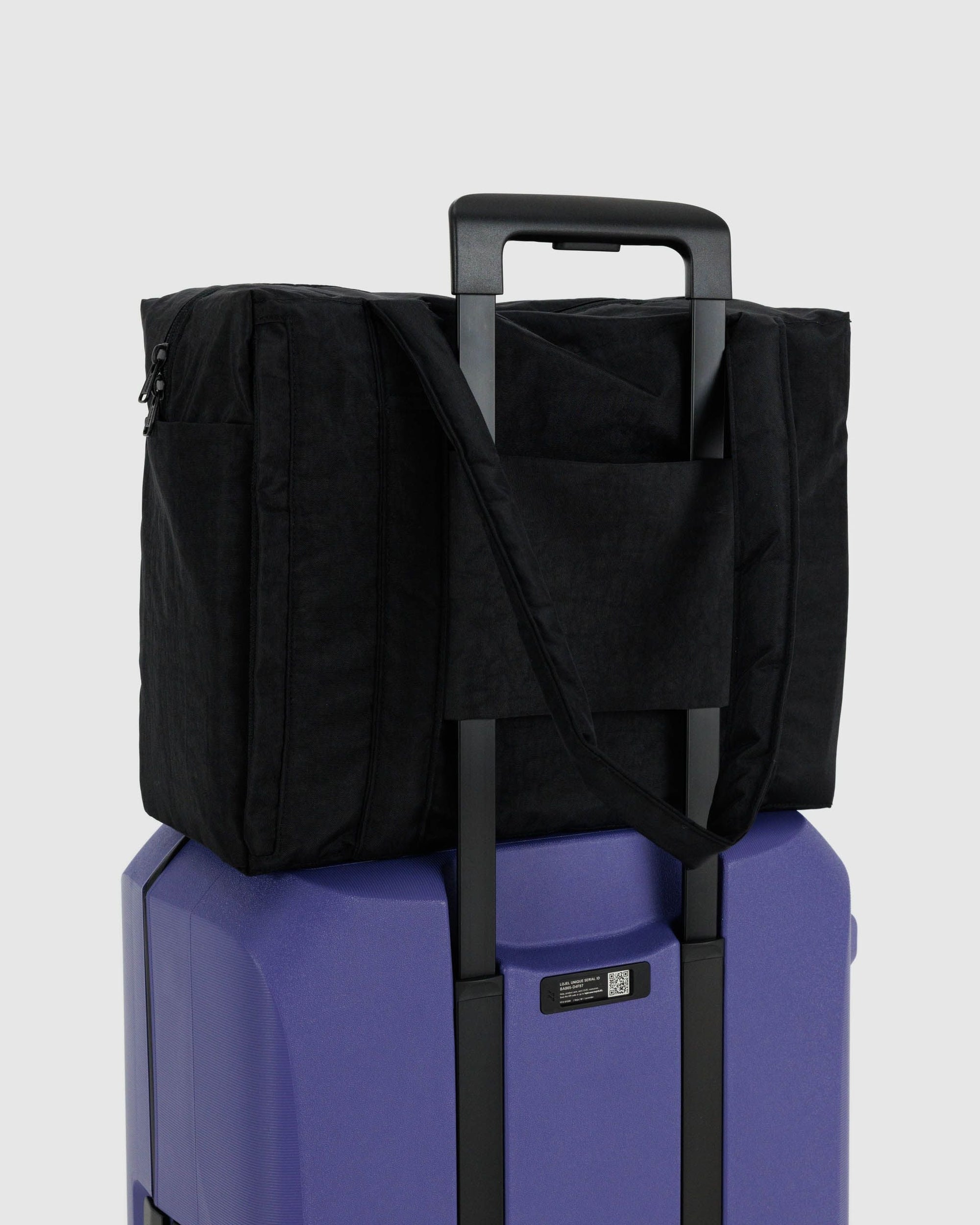 Black quilted carry-on bag with shoulder strap positioned on purple suitcase handle