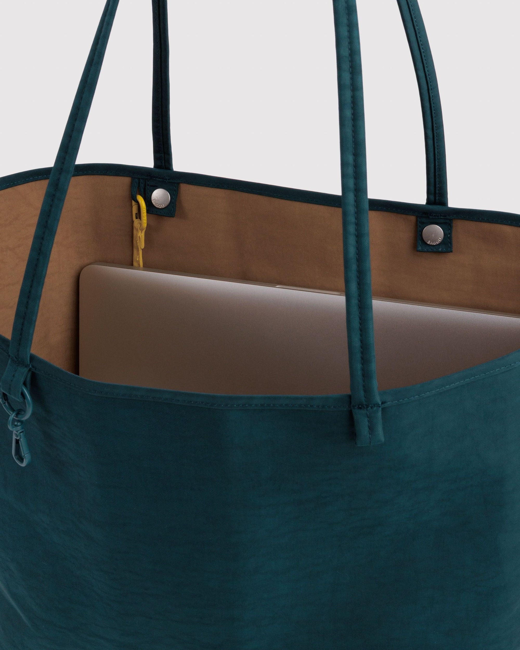 Interior view of teal Baggu reversible nylon tote showing laptop sleeve and tan lining