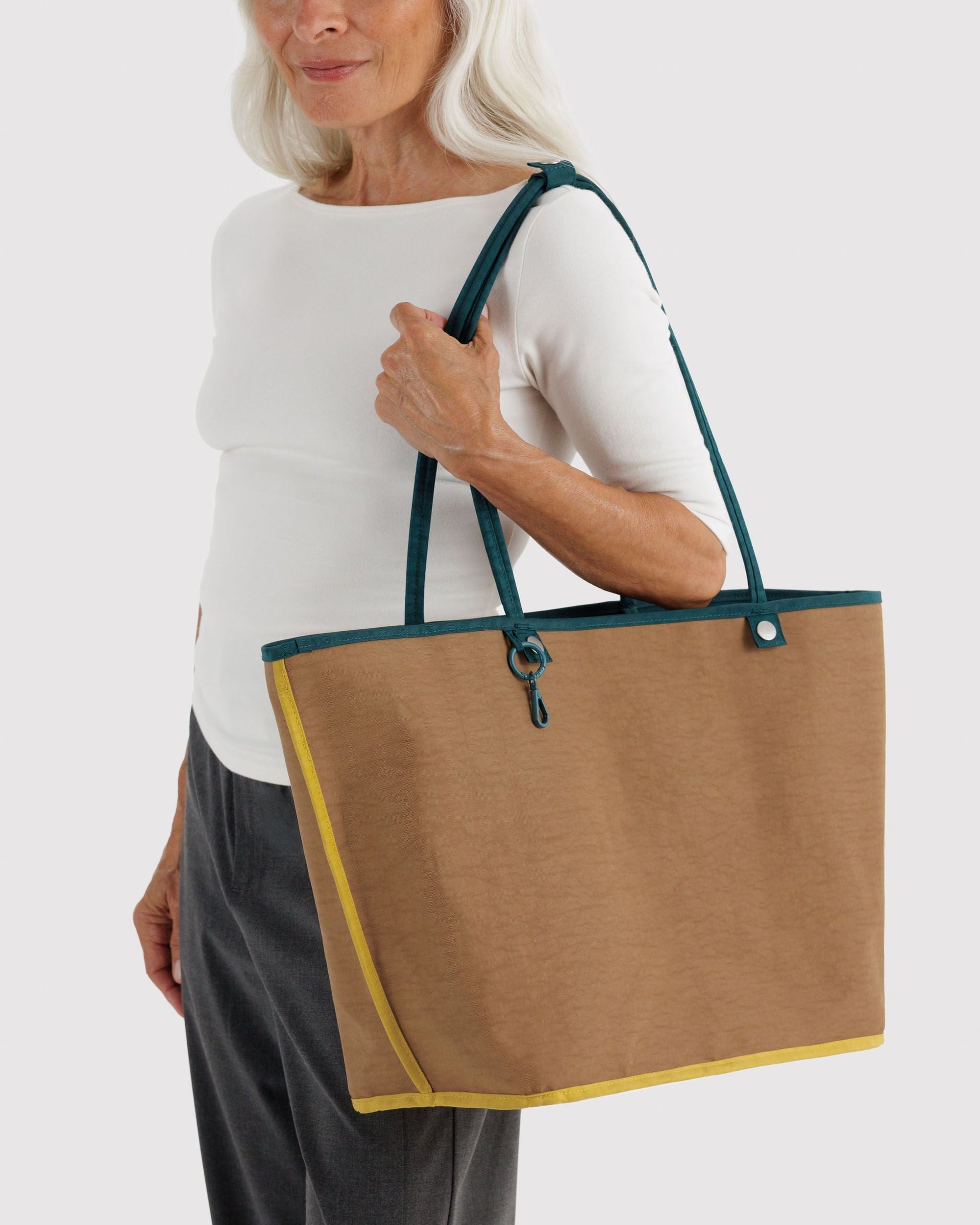Silver-haired woman carrying large tan nylon tote bag with teal handles and yellow trim on shoulder