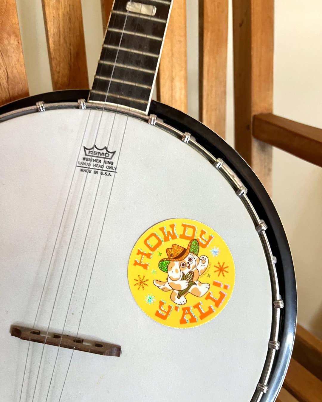 Yellow circular sticker with cowboy dog character saying Howdy Y'all on white banjo drum head