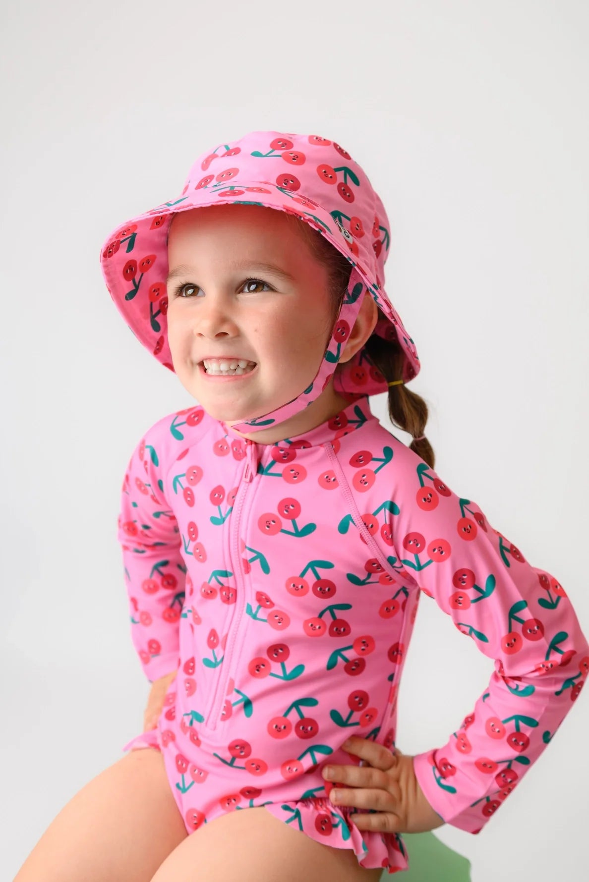 Young girl wearing pink cherry-print long-sleeve rash guard swimsuit and matching bucket hat