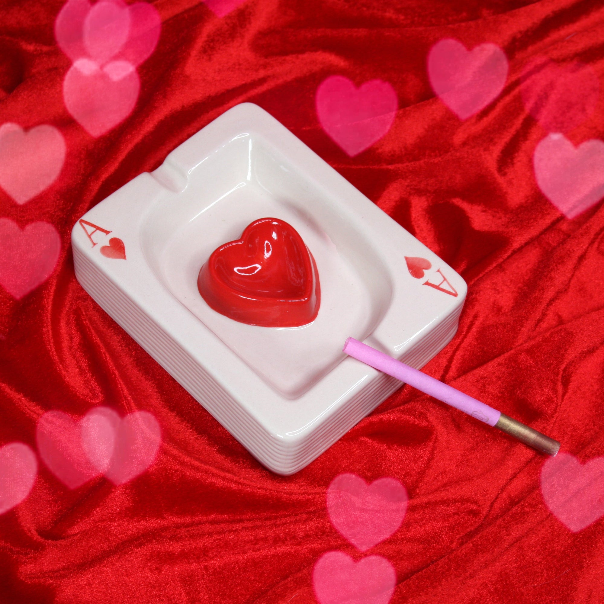 White ceramic ashtray shaped like Ace of Hearts playing card with red heart center and pink cigarette