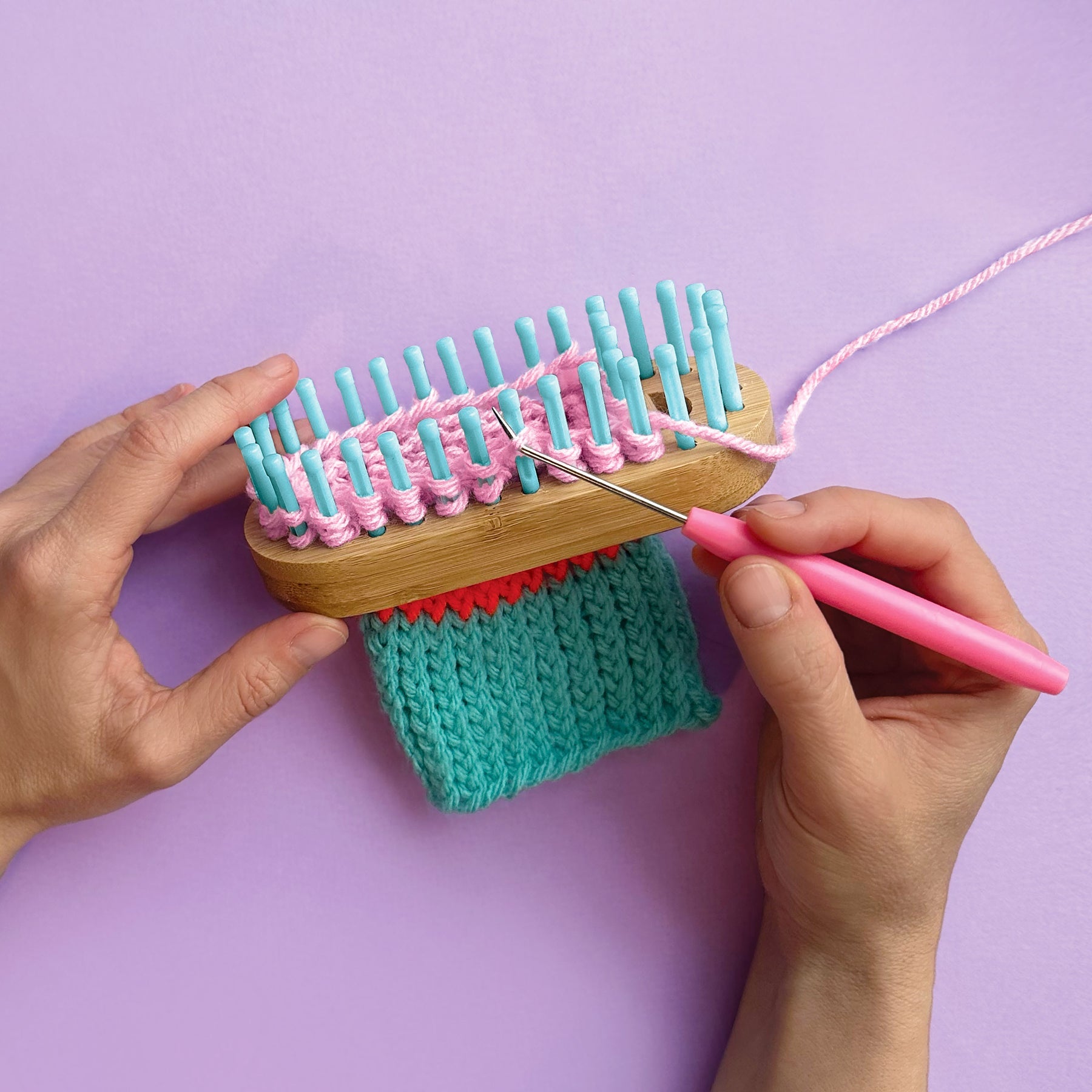 Person using a small knitting loom with pink yarn on a purple background