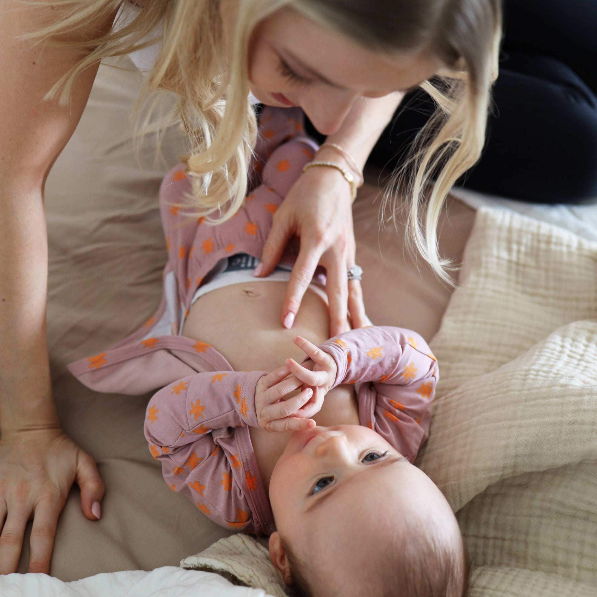 Baby wearing Bonsie Galaxy Gleam footie while parent practices skin-to-skin contact on bed