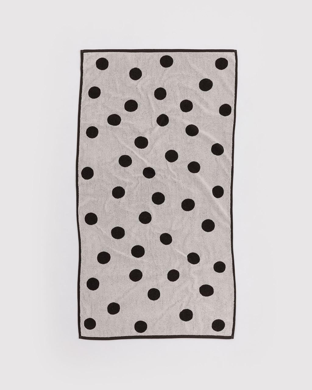 Cream terry bath towel with scattered black polka dots and black border trim