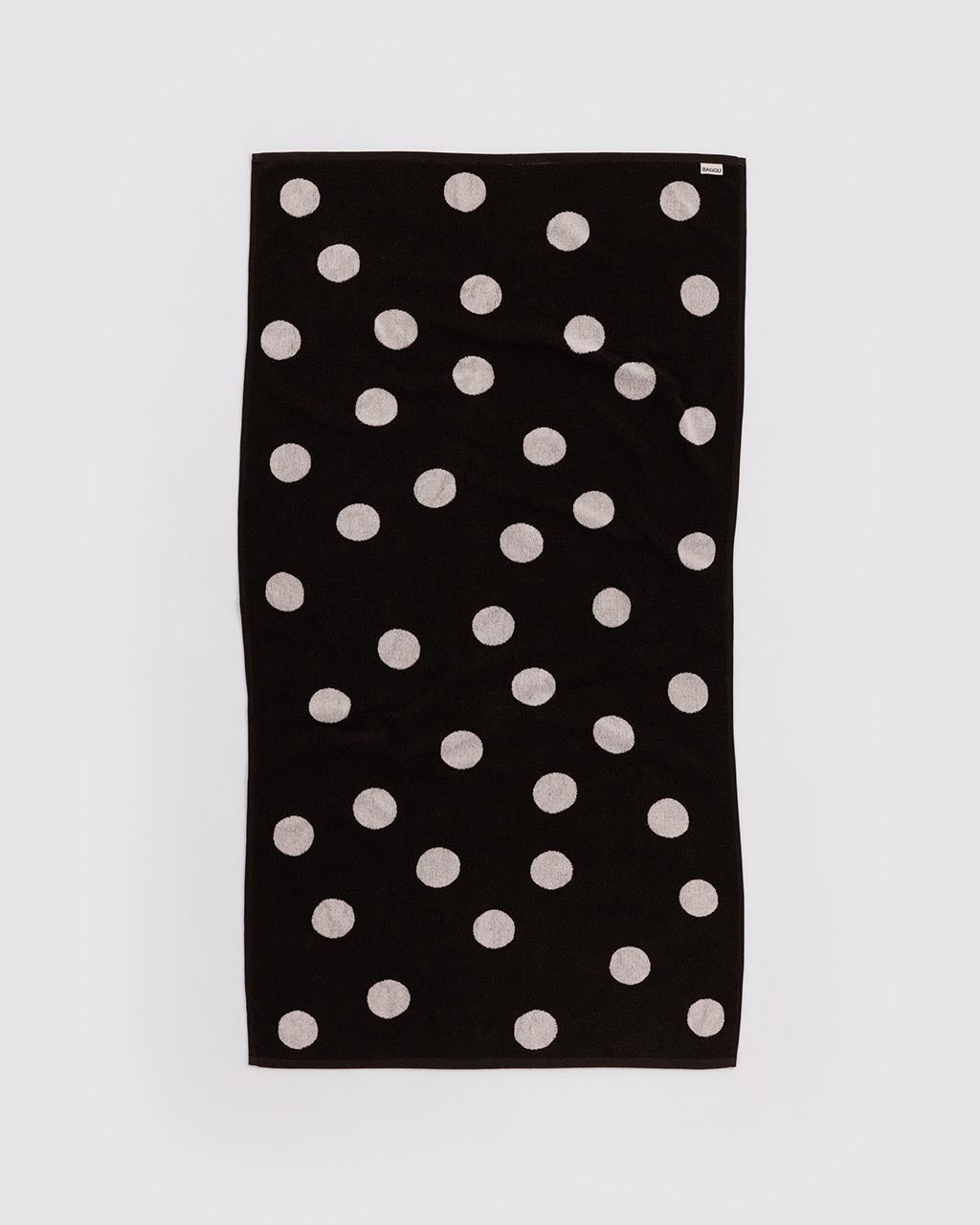 Baggu black bath towel with scattered cream polka dots laid flat on white background