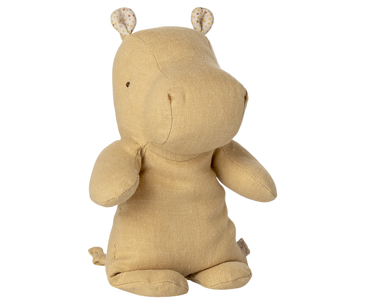Cream yellow stuffed hippo toy with floral patterned ears against wooden slat background