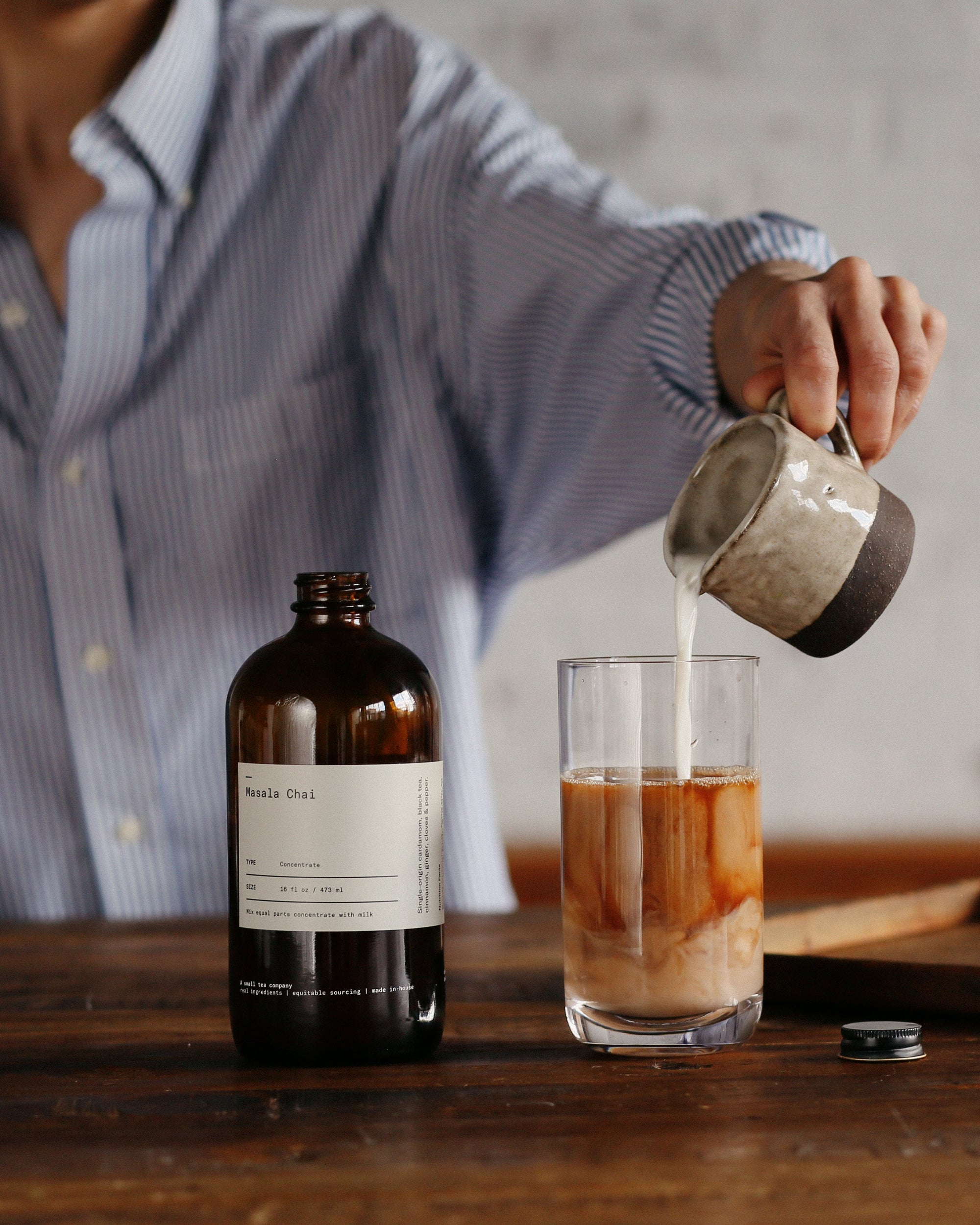 Person pouring milk into glass with Masala Chai concentrate creating layered drink
