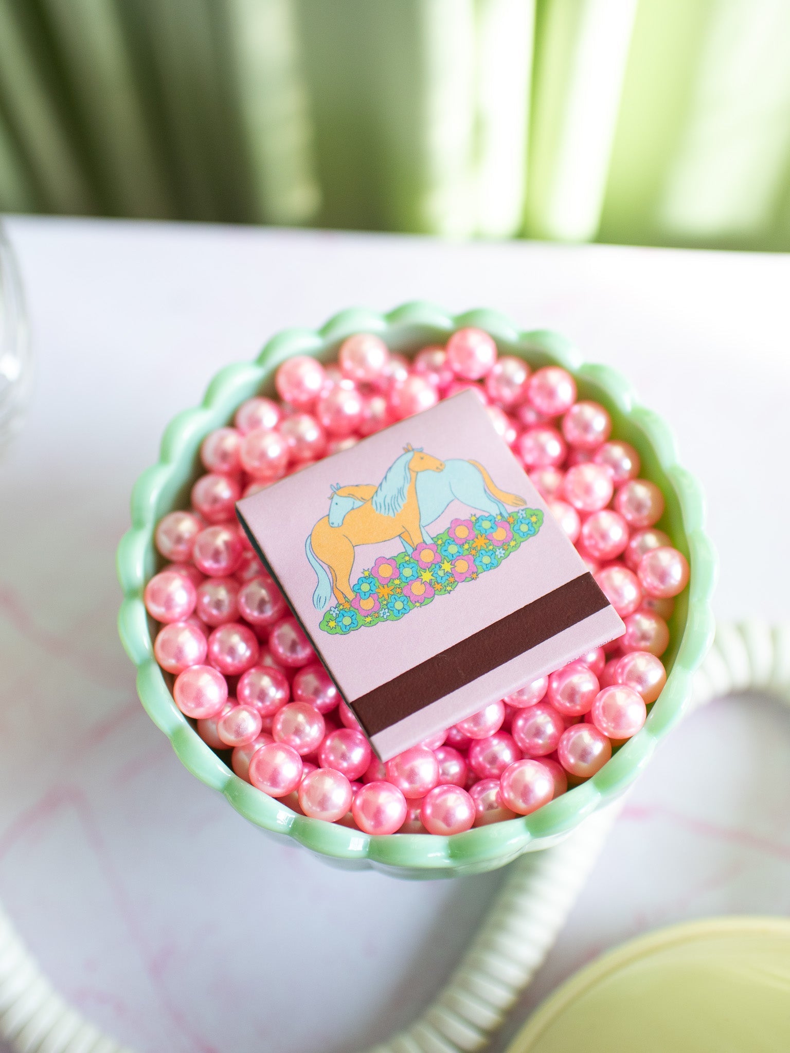 Horse Girl matchbook with unicorn illustration sitting in bowl of pink pearls on white surface