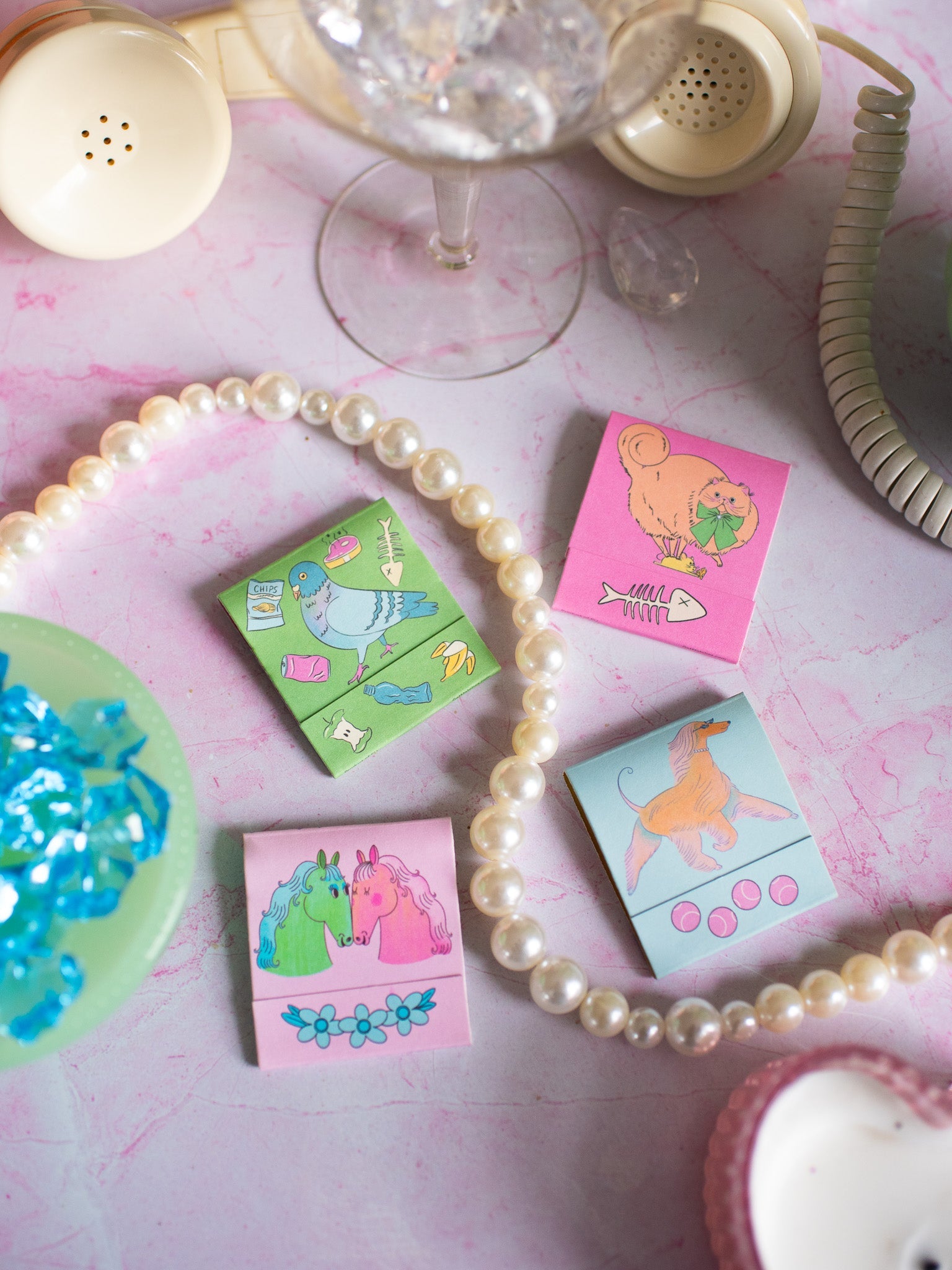 Colorful horse-themed matchbook stickers displayed with vintage phone and pearl necklace on marble surface