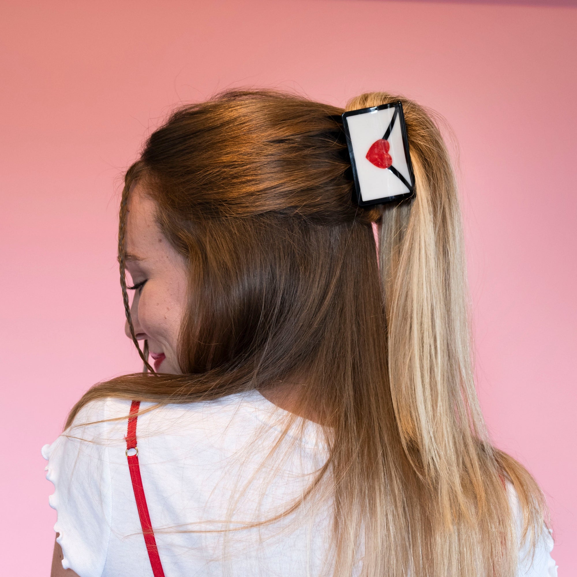 Woman wearing white rectangular hair claw with red heart design in blonde hair against pink background