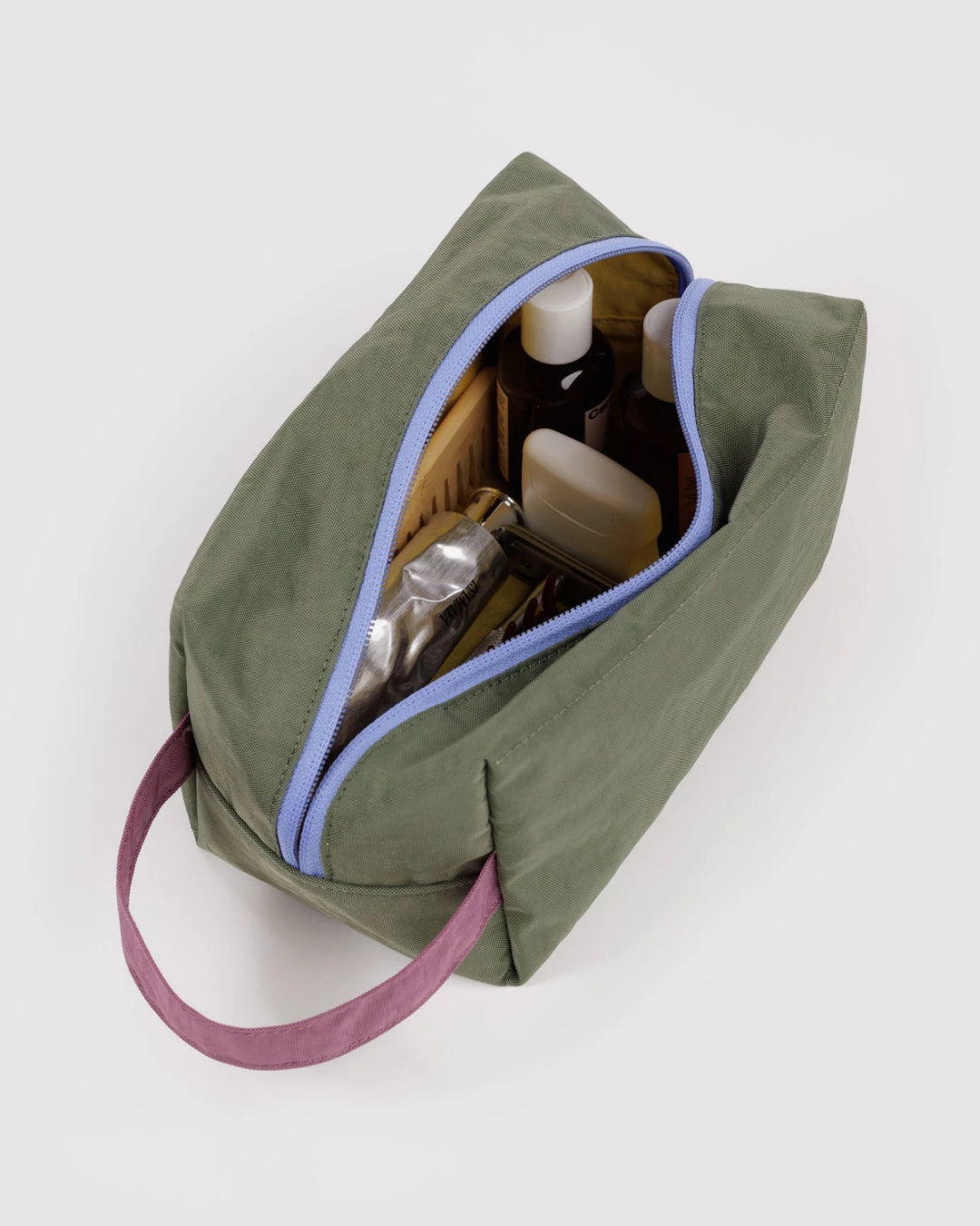 Open olive green Baggu Dopp Kit with periwinkle zipper and plum handle, filled with toiletries