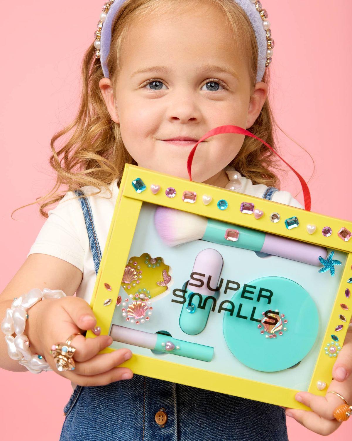 Child holding a 'Super Smalls' toy set against a pink background