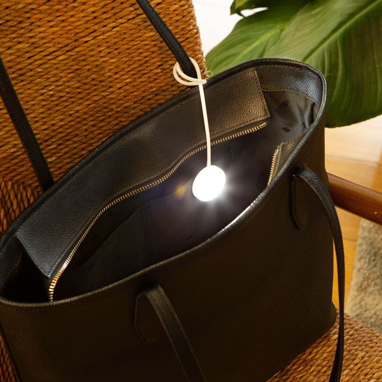 Small glowing white ball purse light hanging inside an open black leather tote bag