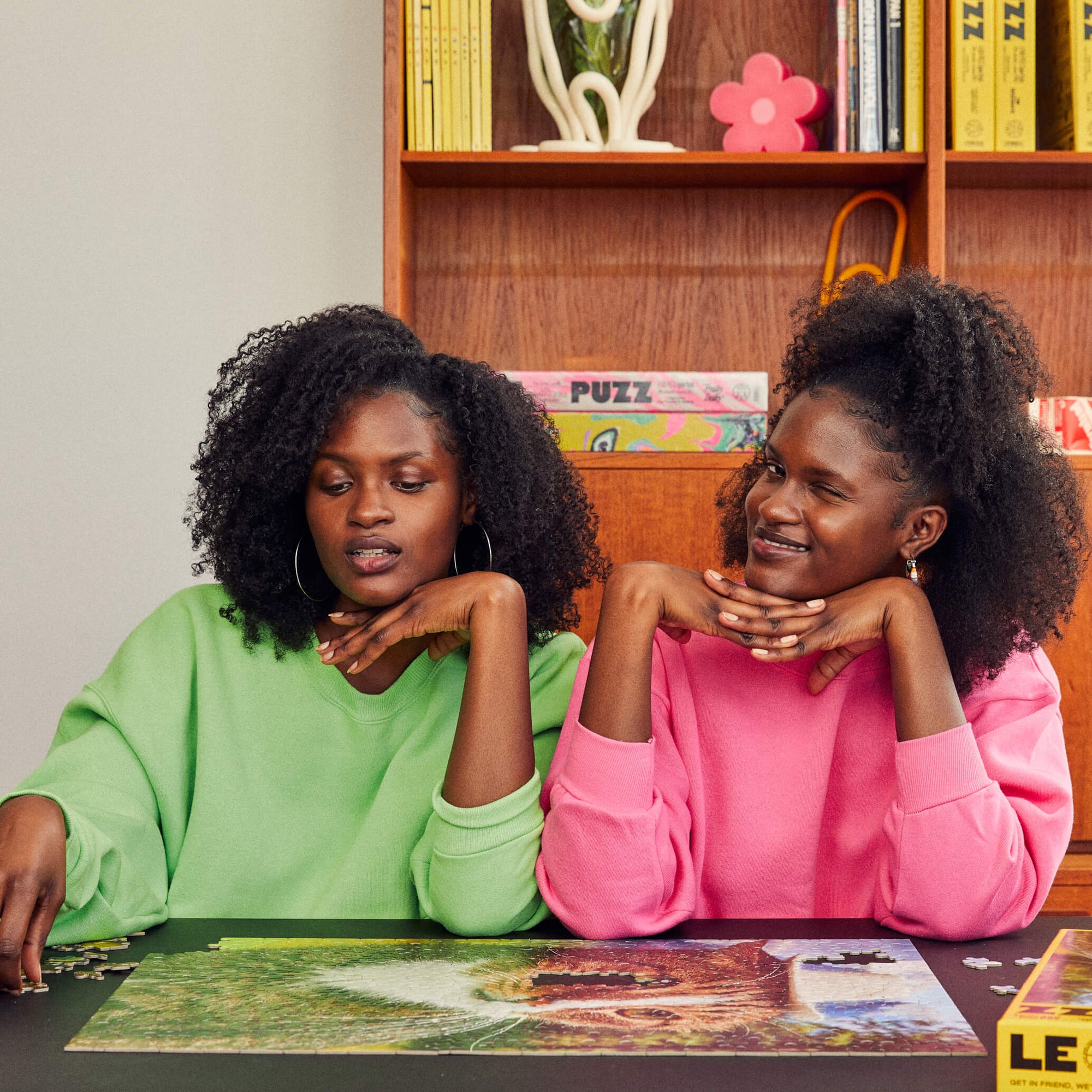 Two women in colorful sweatshirts assemble a Le Puzz jigsaw puzzle at a table