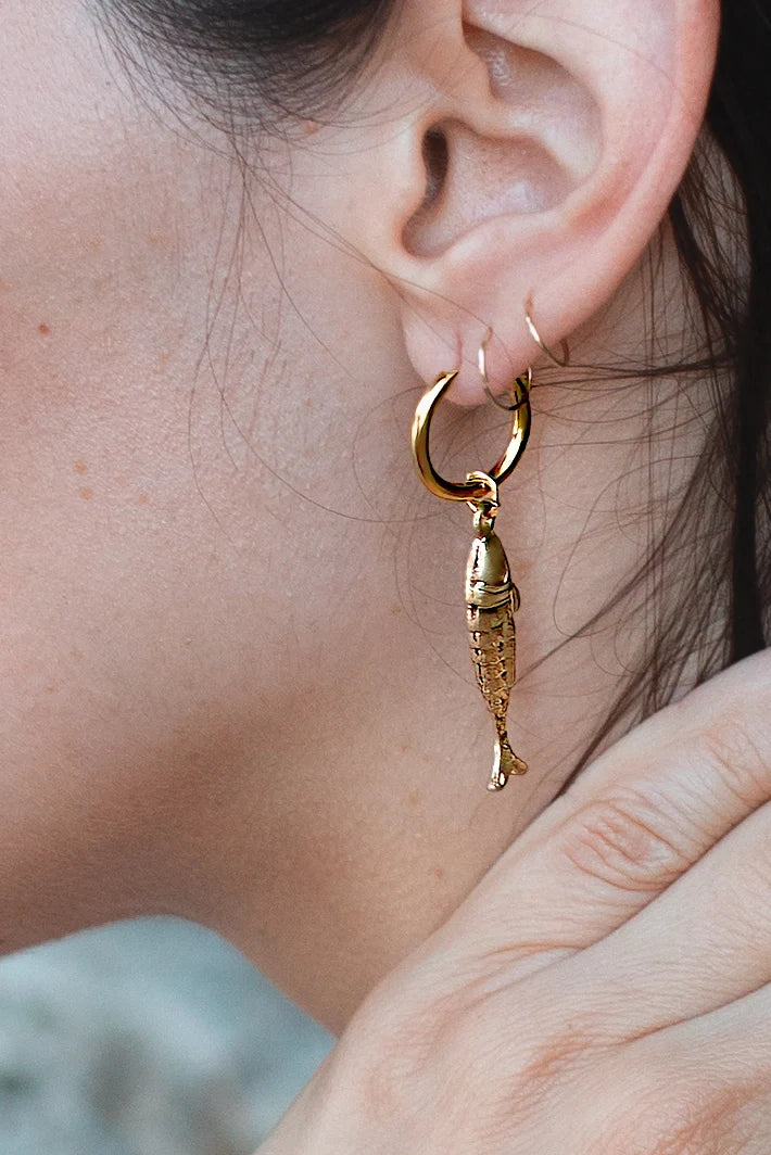 Model wearing gold hoop earring with detailed fish charm pendant by Peter and June