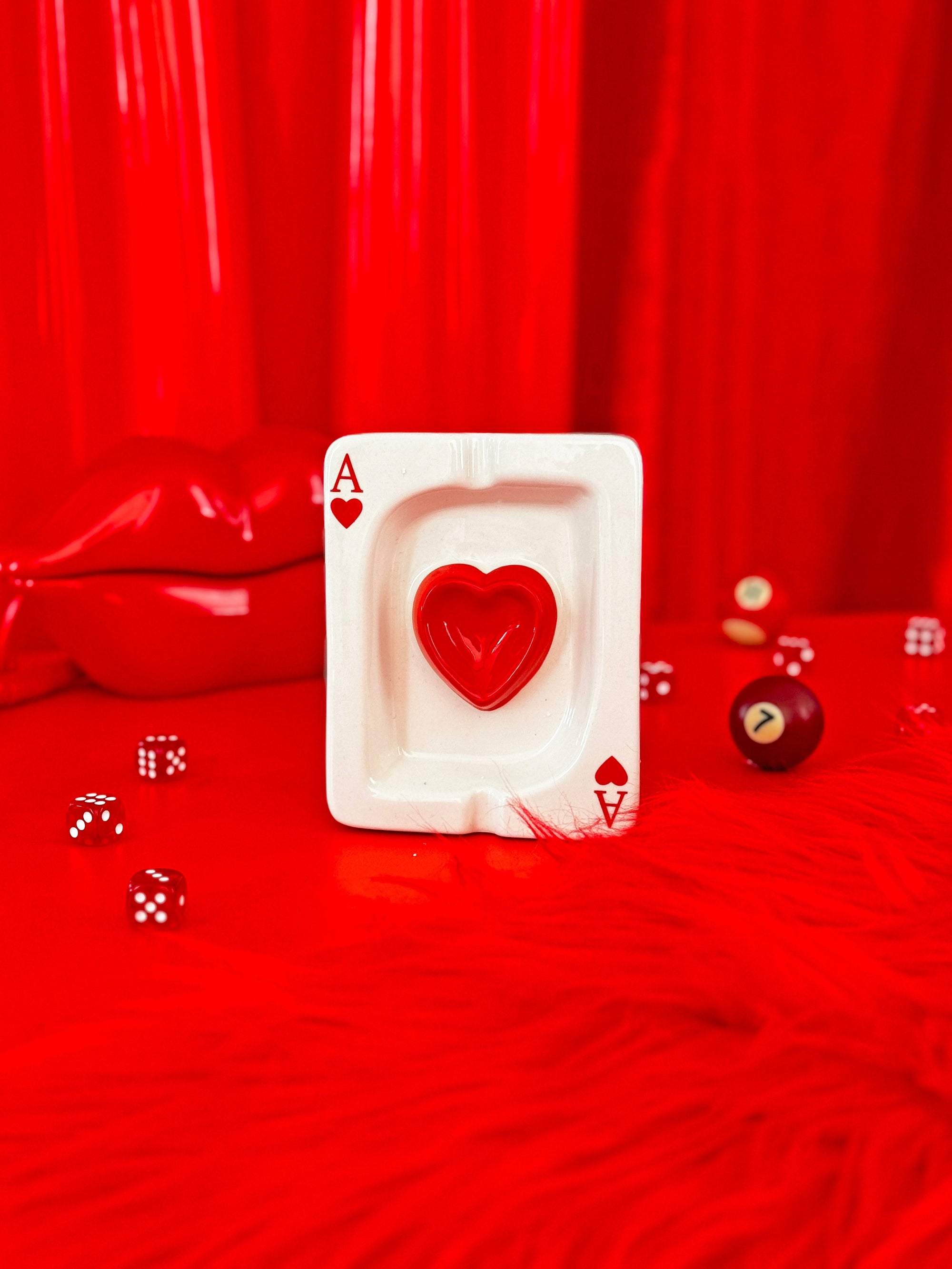 Red ace of hearts playing card ashtray on glossy red surface with dice