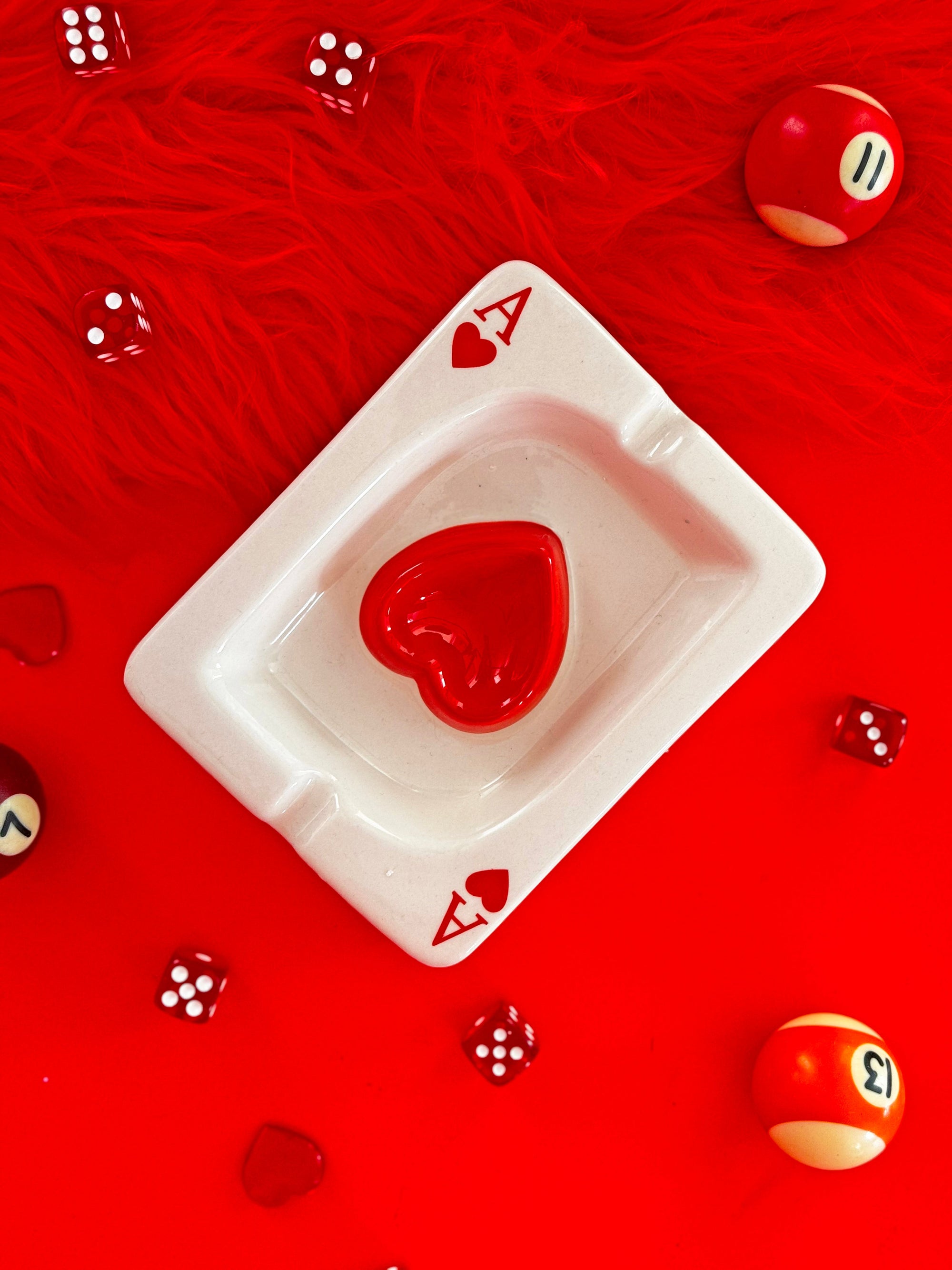 White ceramic Ace of Hearts playing card shaped ashtray with red heart design on red background