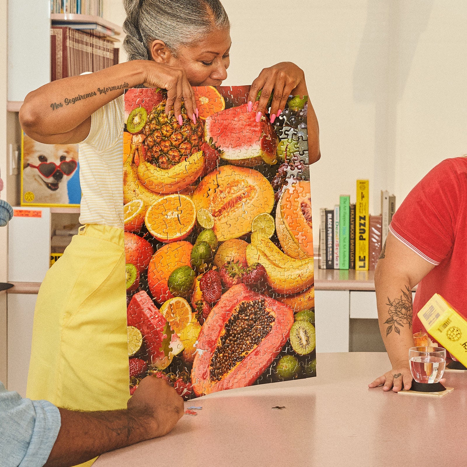 Woman holding completed Le Puzz 'Juicy' fruit-themed jigsaw puzzle showing tropical fruits