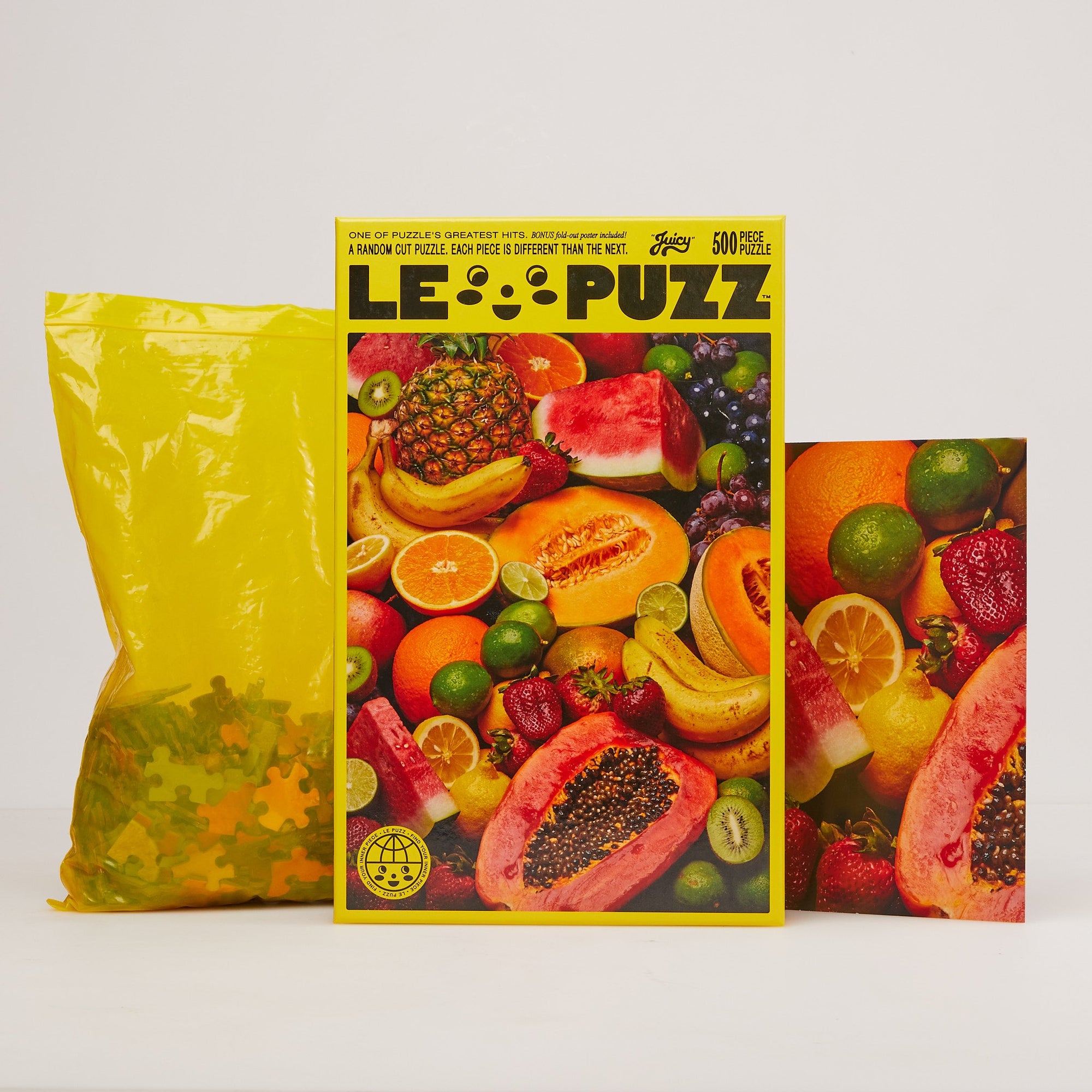 Le Puzz Juicy 500-piece random cut puzzle box with fruit imagery, yellow bag, and reference poster