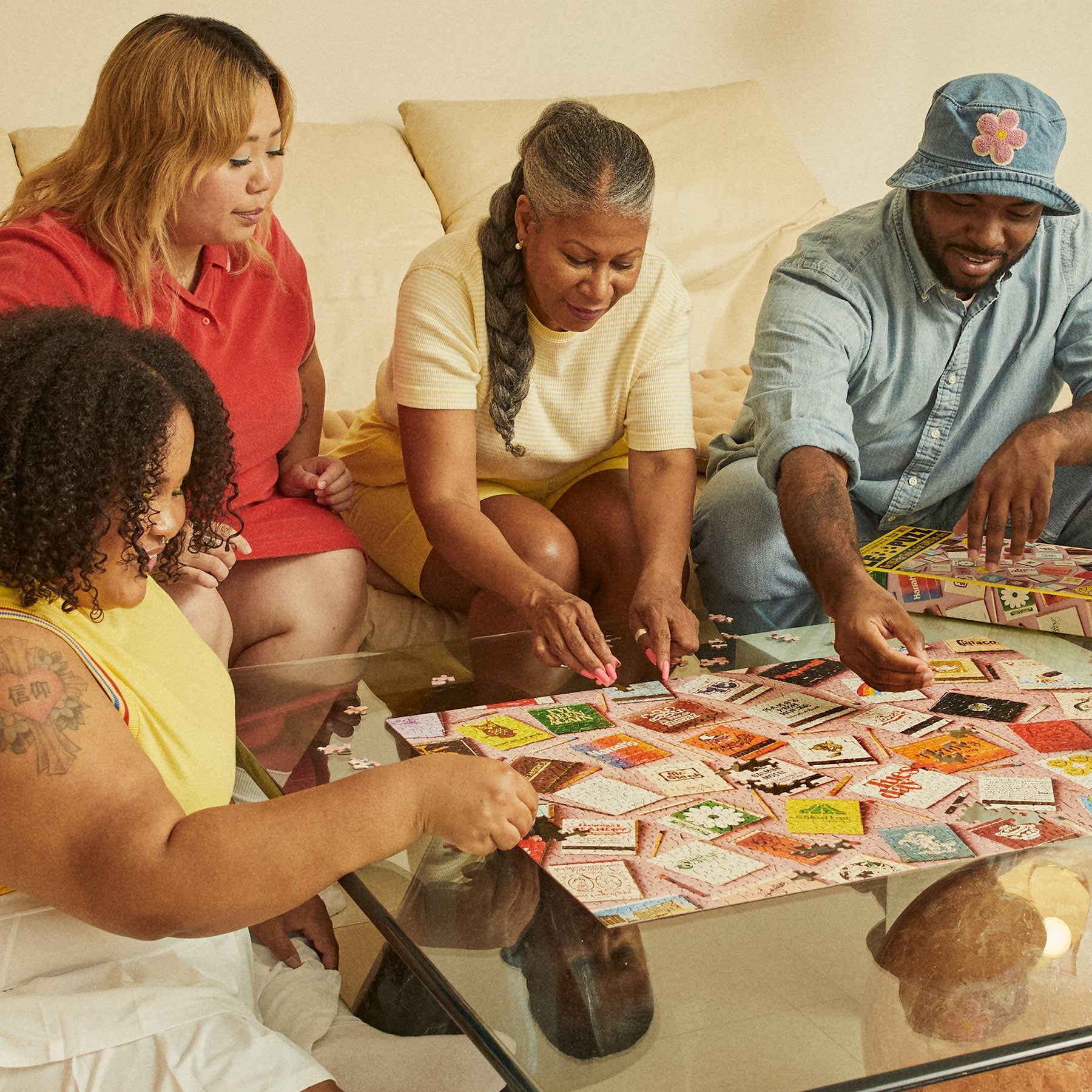 Four people gathered around a glass coffee table assembling the Le Puzz Match Made in Heaven jigsaw puzzle