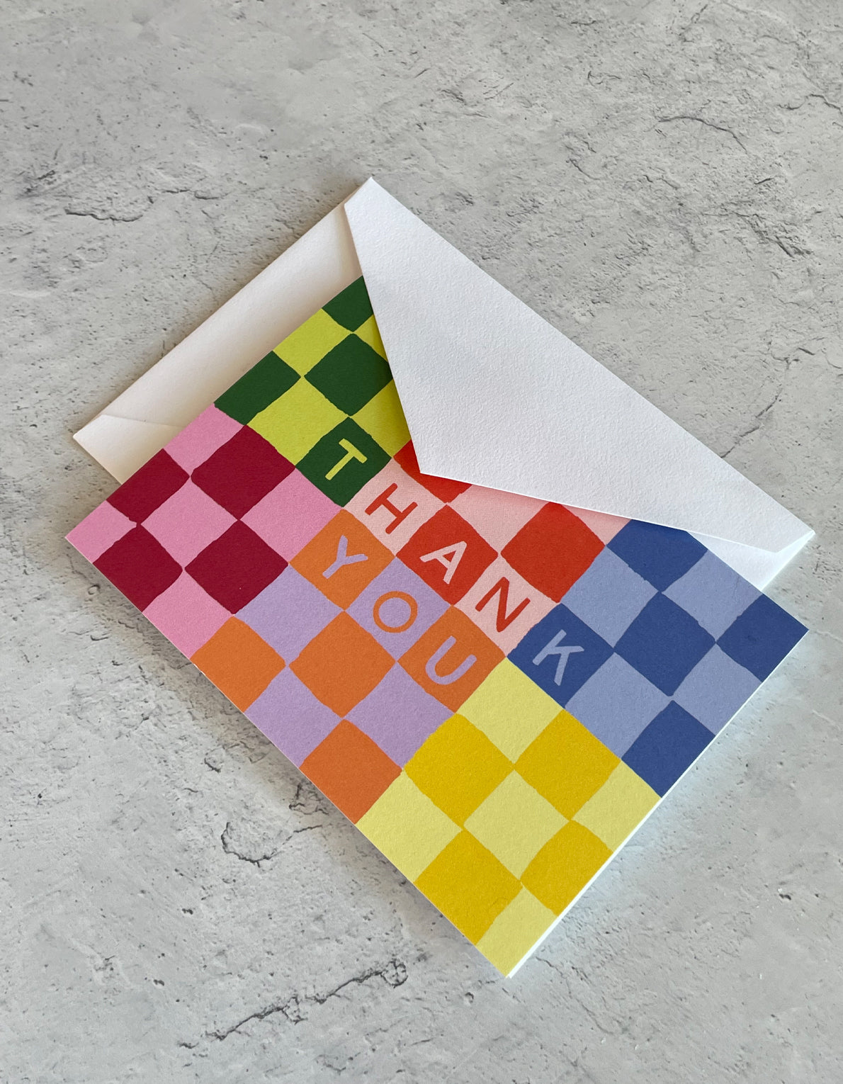 Colorful checkerboard pattern thank you notecard with white envelope on concrete surface