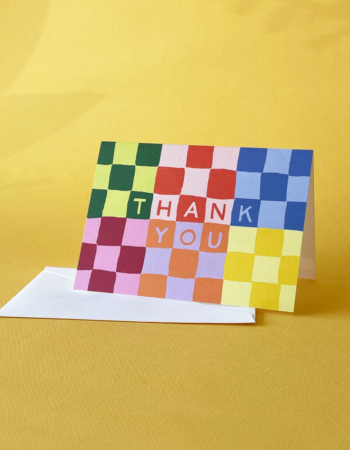 Colorful checkerboard pattern thank you notecard with white envelope on yellow background
