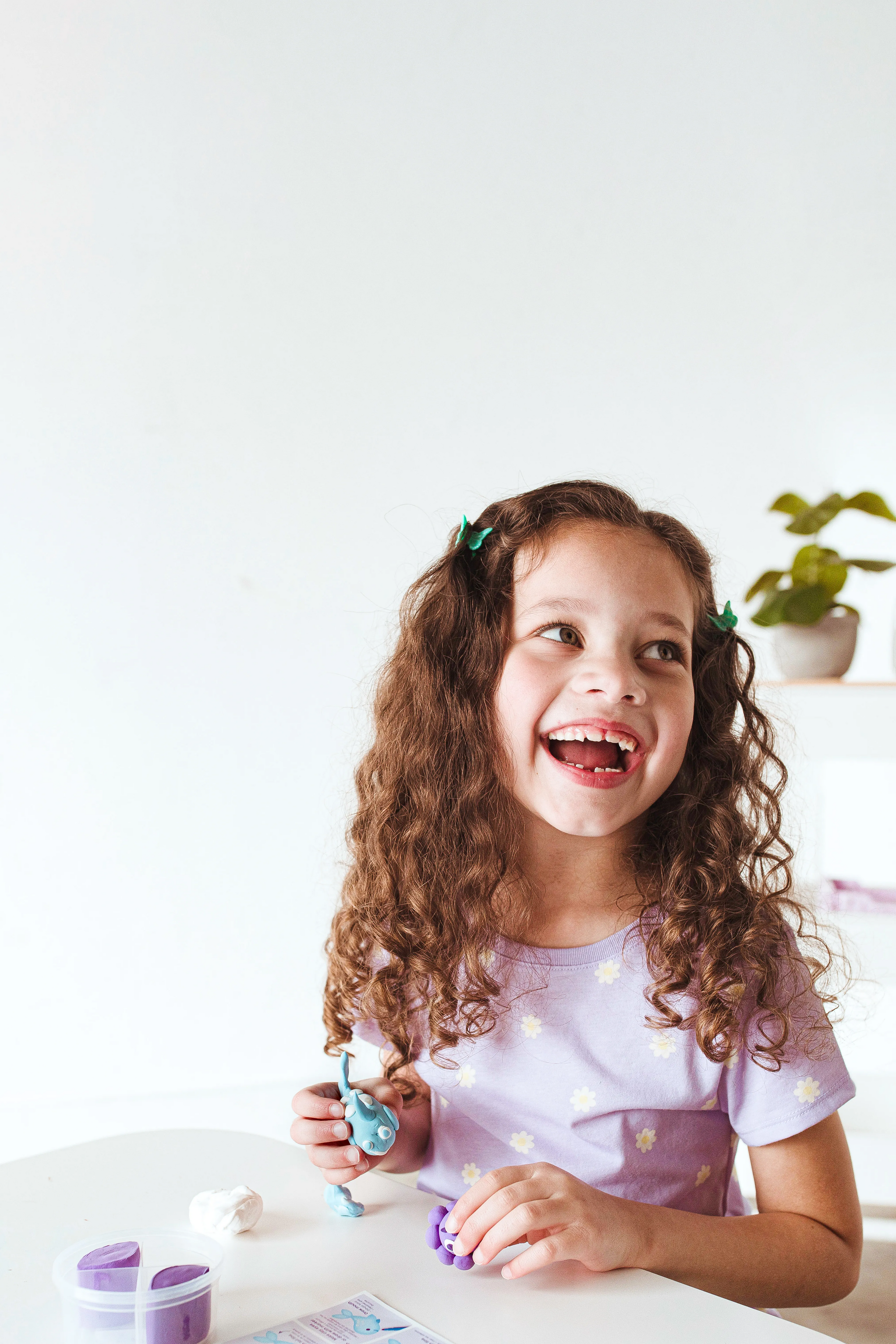 Happy child with curly hair using colorful air-dry clay crafting kit at table