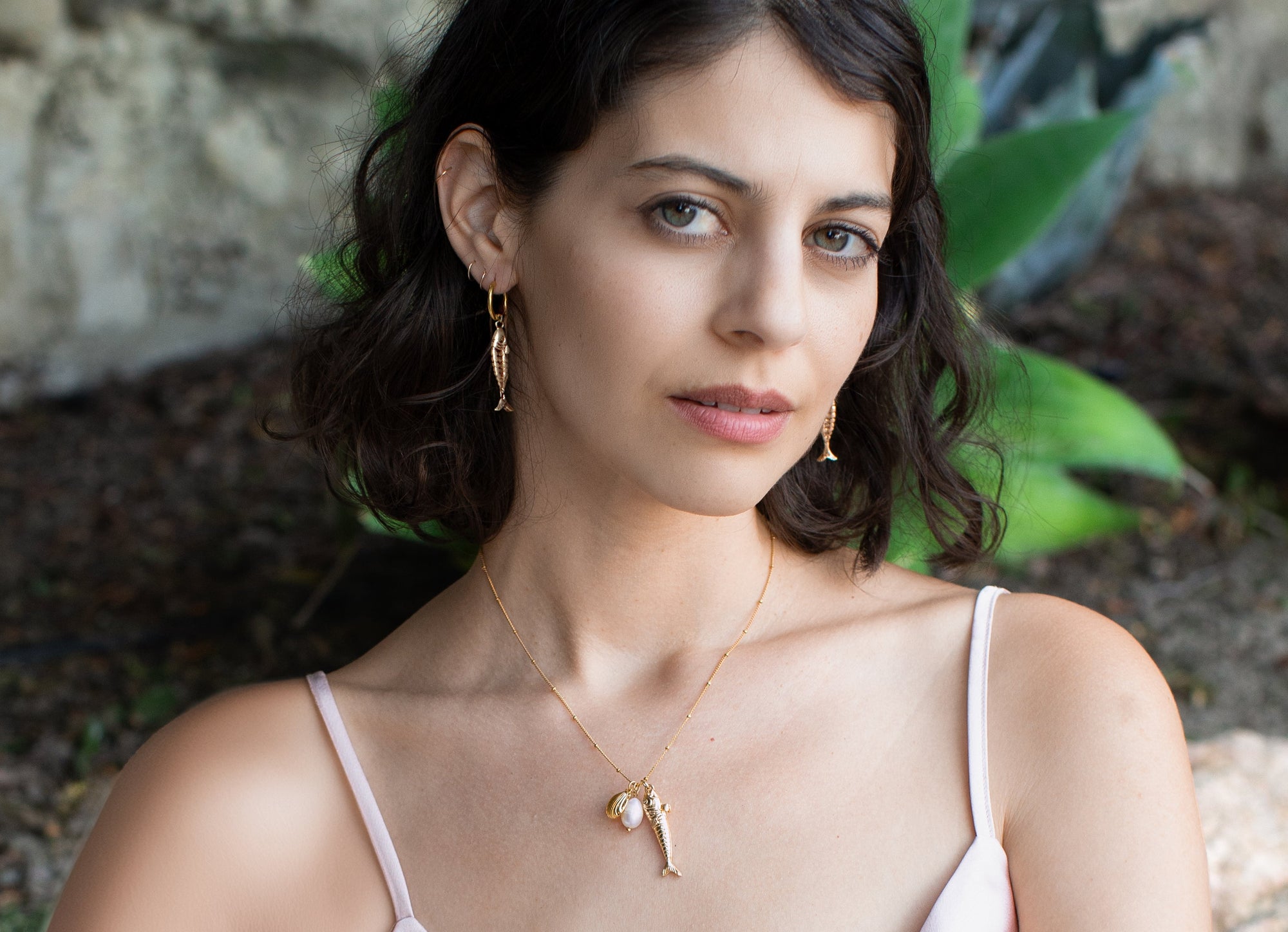 Model wearing gold fish-shaped hoop earrings with matching necklace outdoors