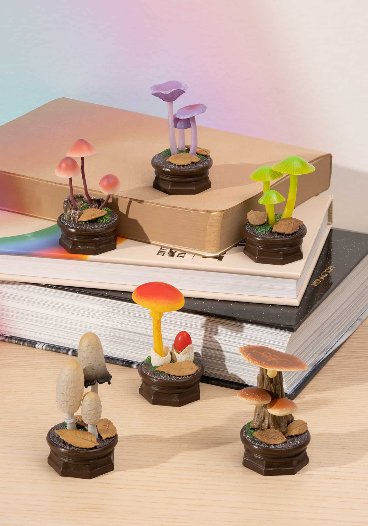 Six miniature mushroom figurines in various colors displayed on decorative bases atop stacked books