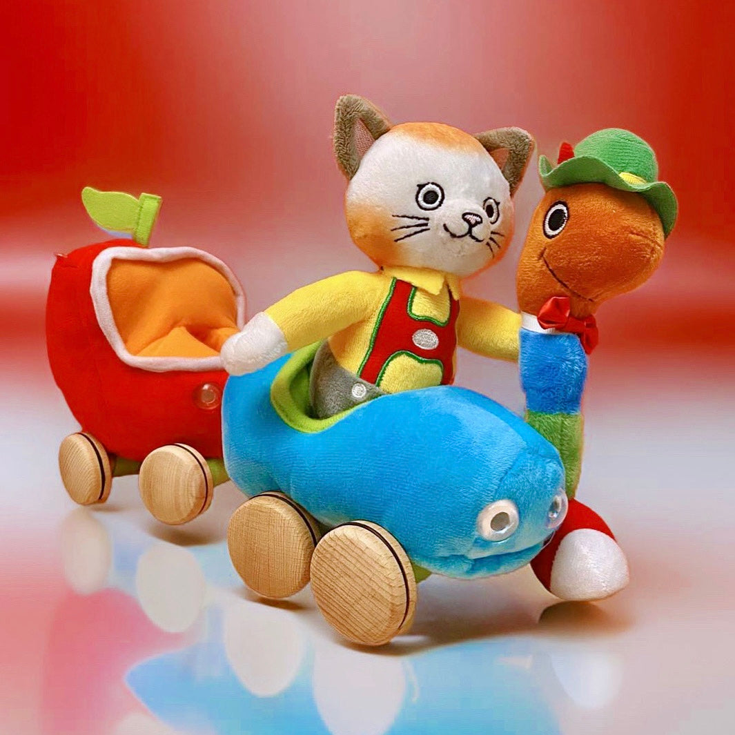 Huckle Cat plush toy riding a blue car with a red apple wagon trailer on wooden wheels