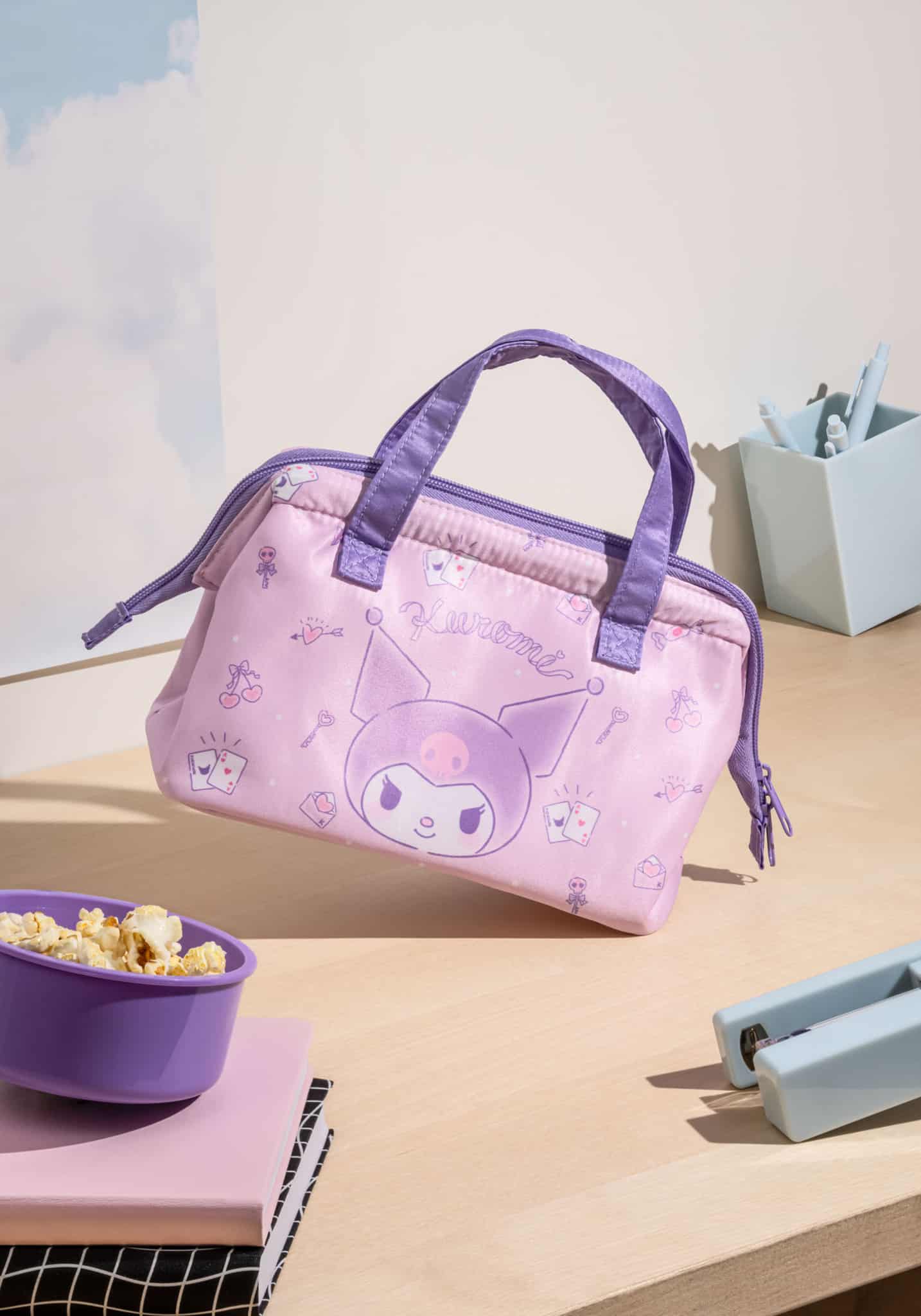 Pink Kuromi insulated lunch tote bag with purple handles on wooden surface with lunch items
