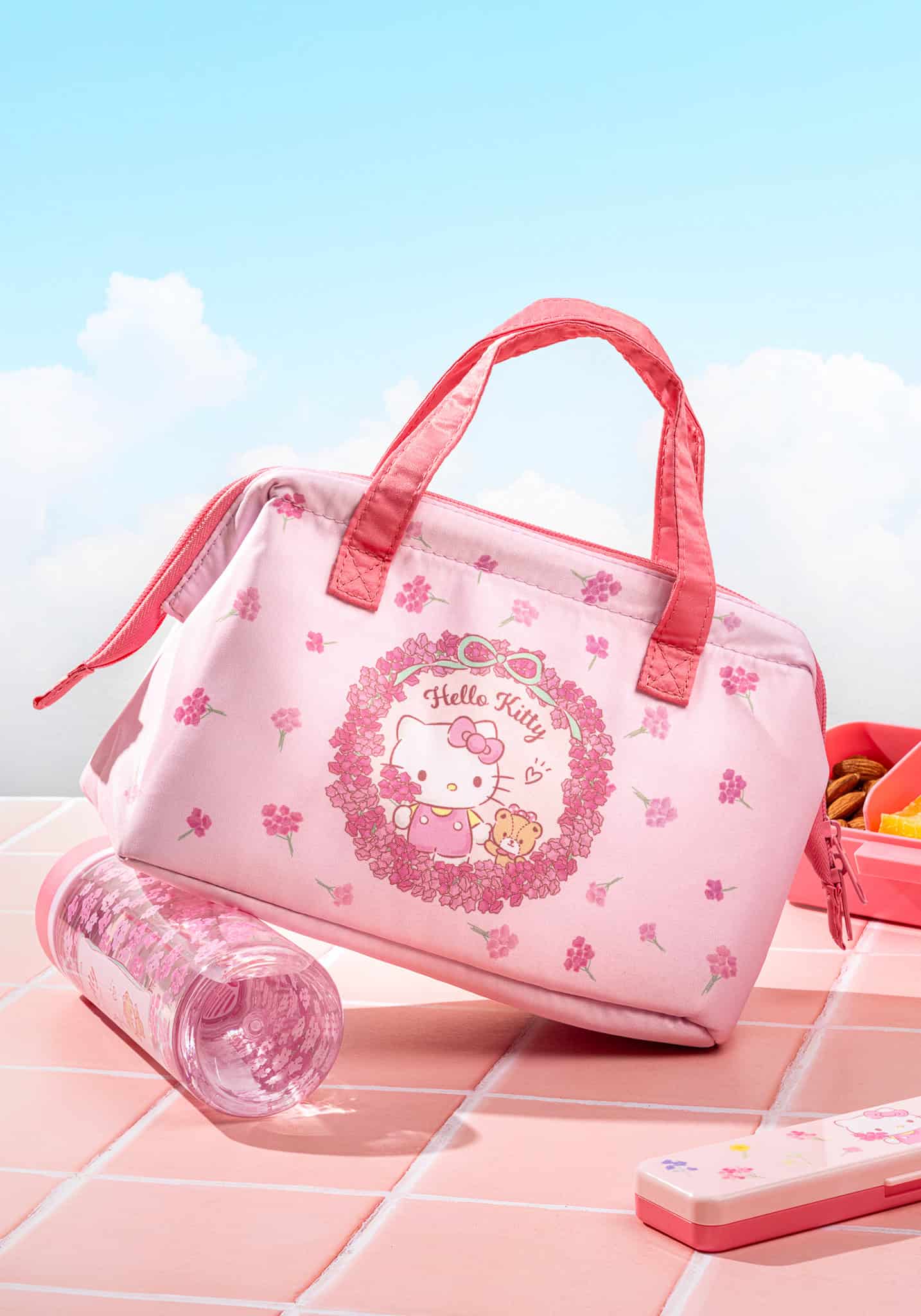 Pink Hello Kitty insulated lunch bag with floral pattern and water bottle on tiled surface
