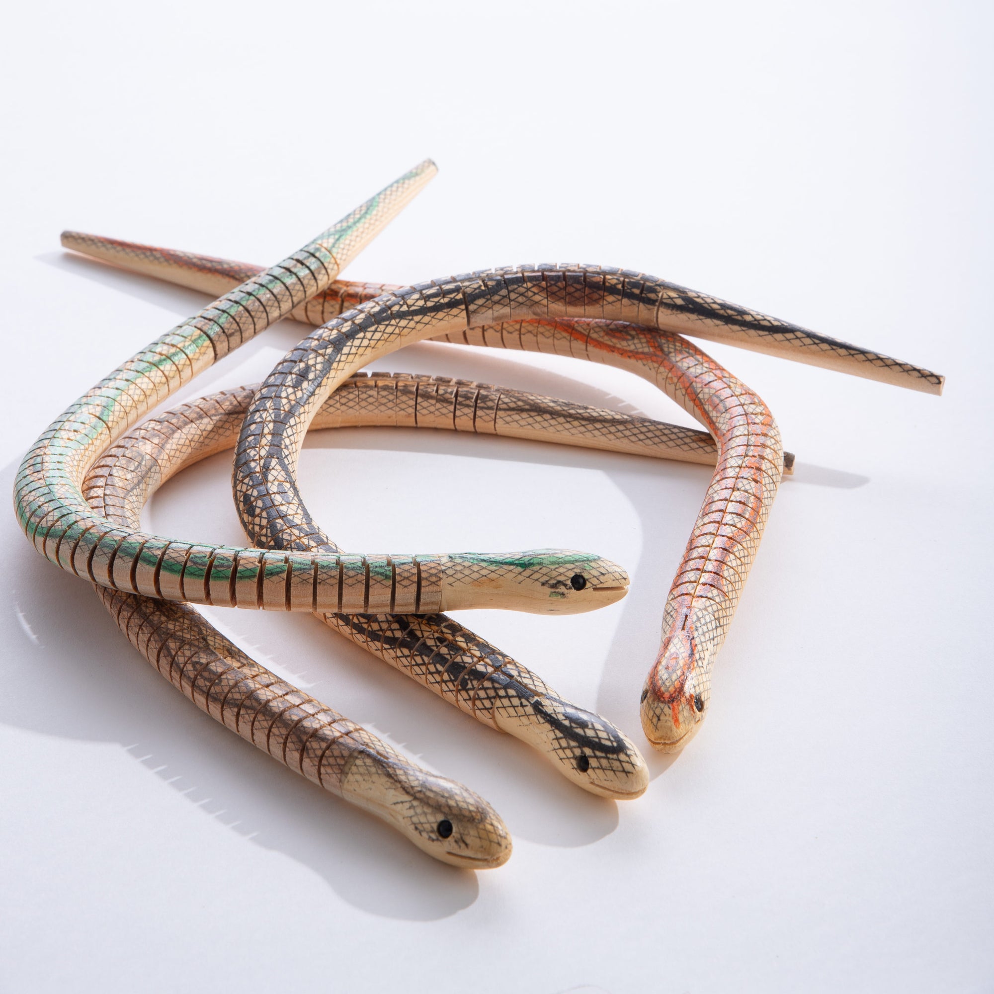 Three wooden painted king snake toys with detailed scale patterns in green, gray, and orange colorways
