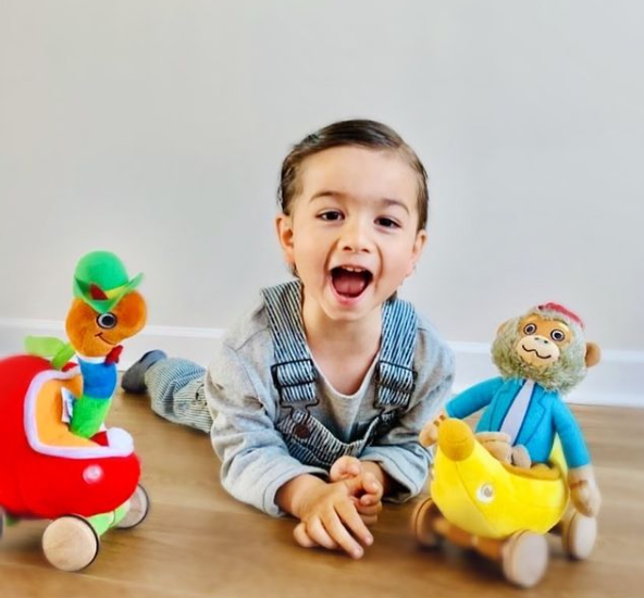 Young child smiling with Yottoy Bananas Gorilla plush toy and yellow Bananamobile on floor