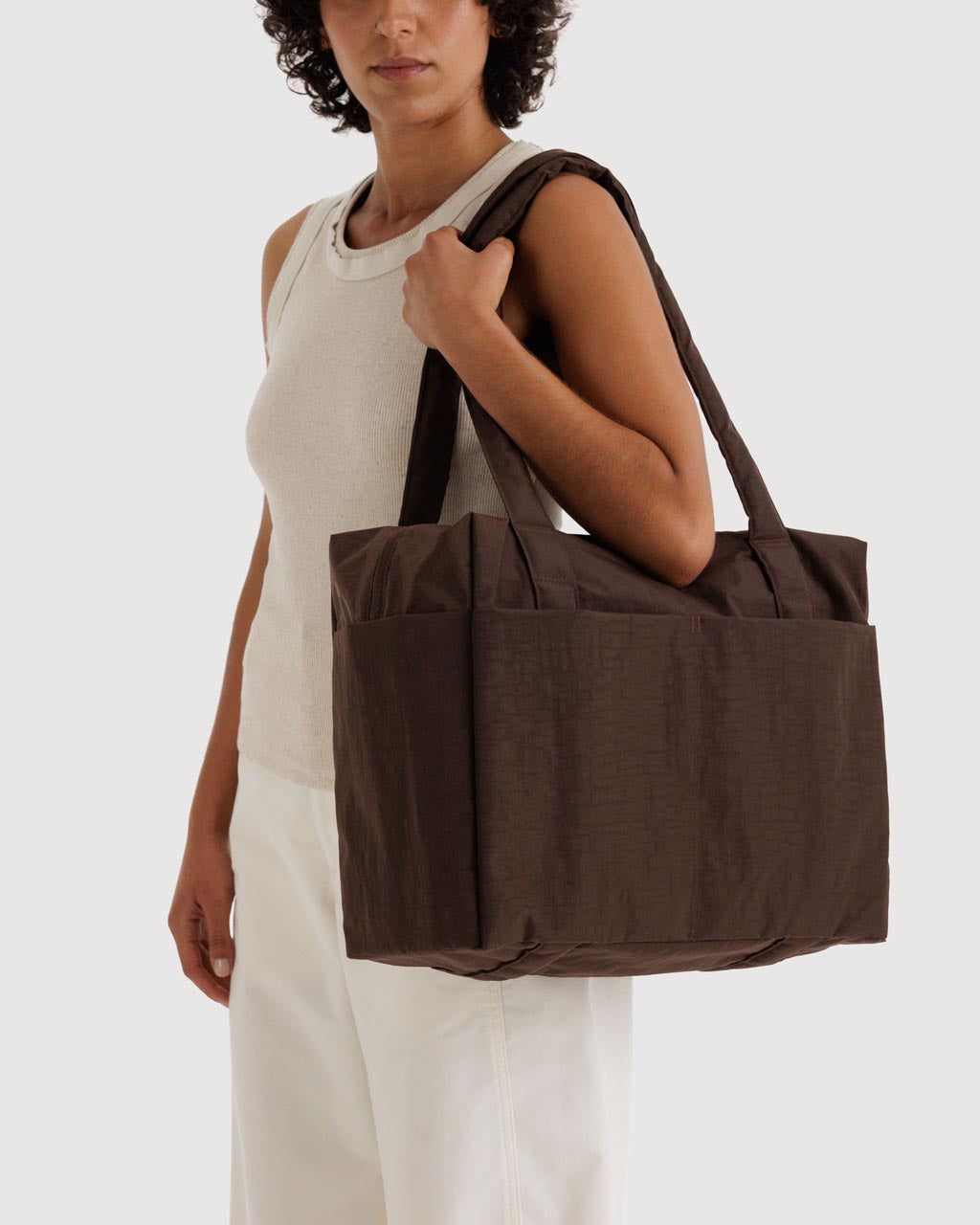 Model carrying large dark brown Baggu Cloud Carry-On tote bag over shoulder