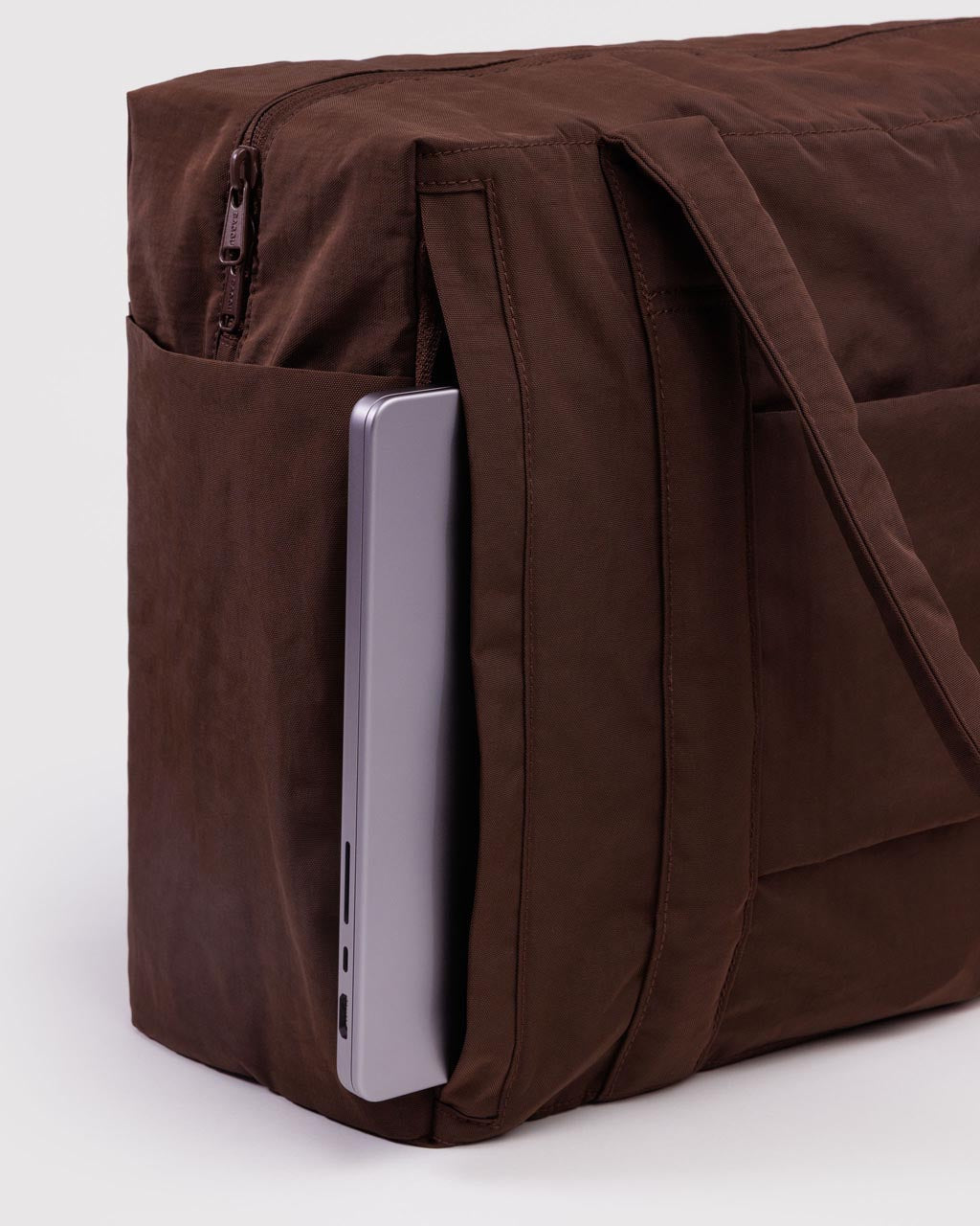 Close-up of brown Baggu Cloud Carry-On bag with laptop in side pocket