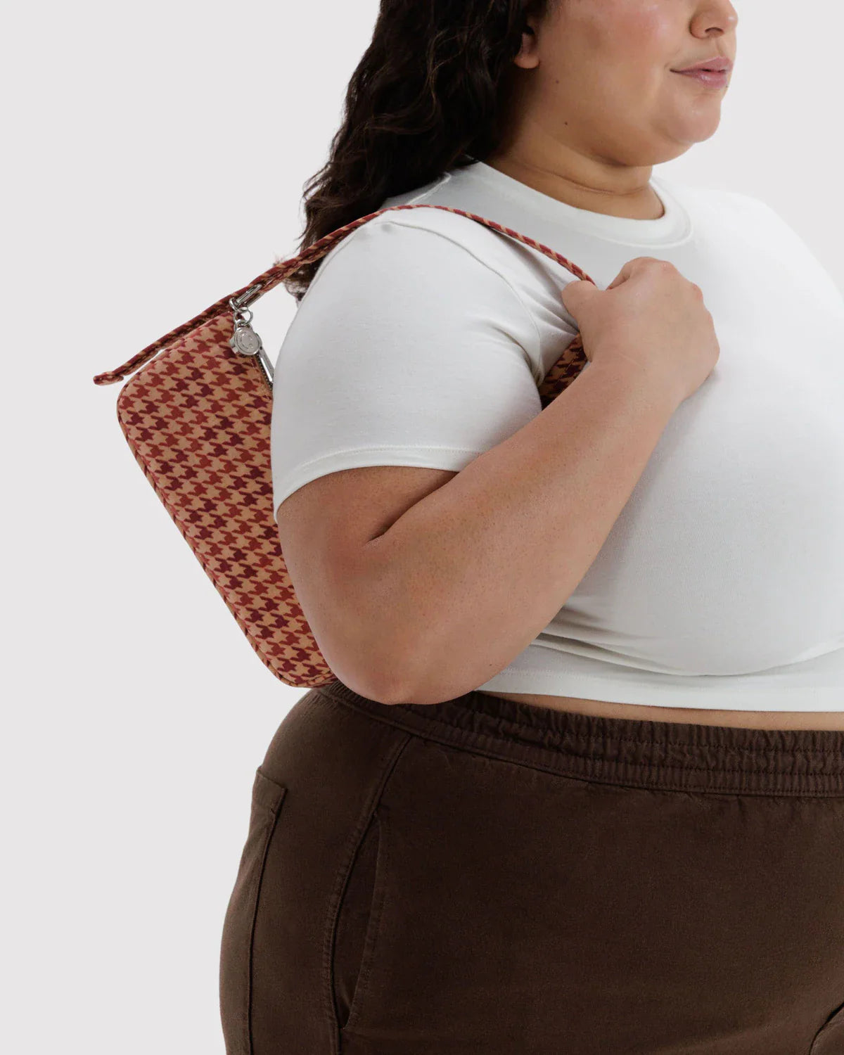 Model carrying Baggu Nylon Pochette in tan and red houndstooth pattern under arm