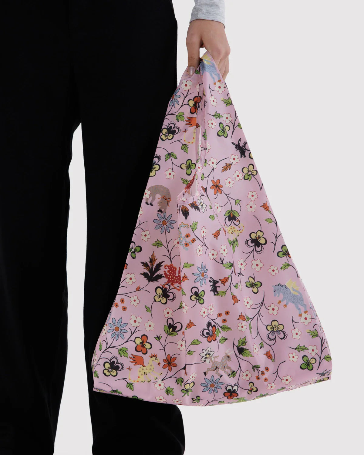 Model holding pink floral Castle Creatures Standard Baggu reusable tote bag with animal motifs