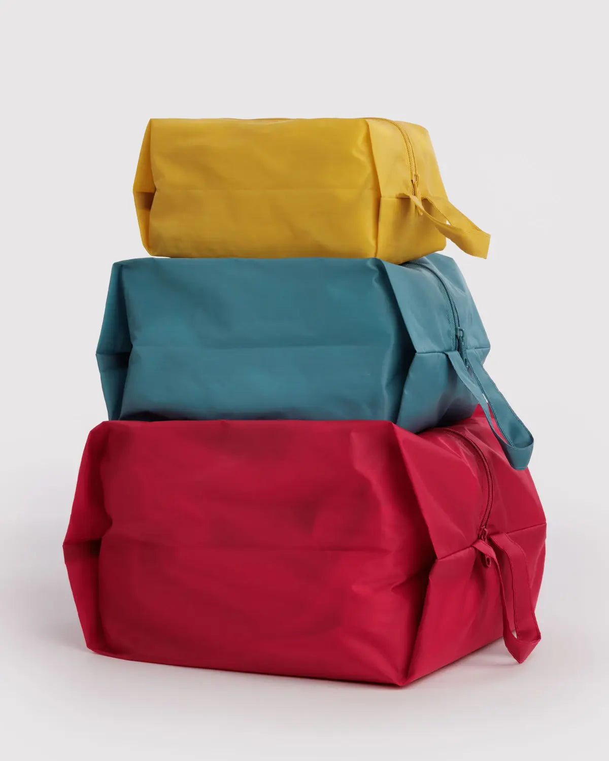 Three Baggu zip pouches stacked in mustard yellow, teal blue, and crimson red sizes